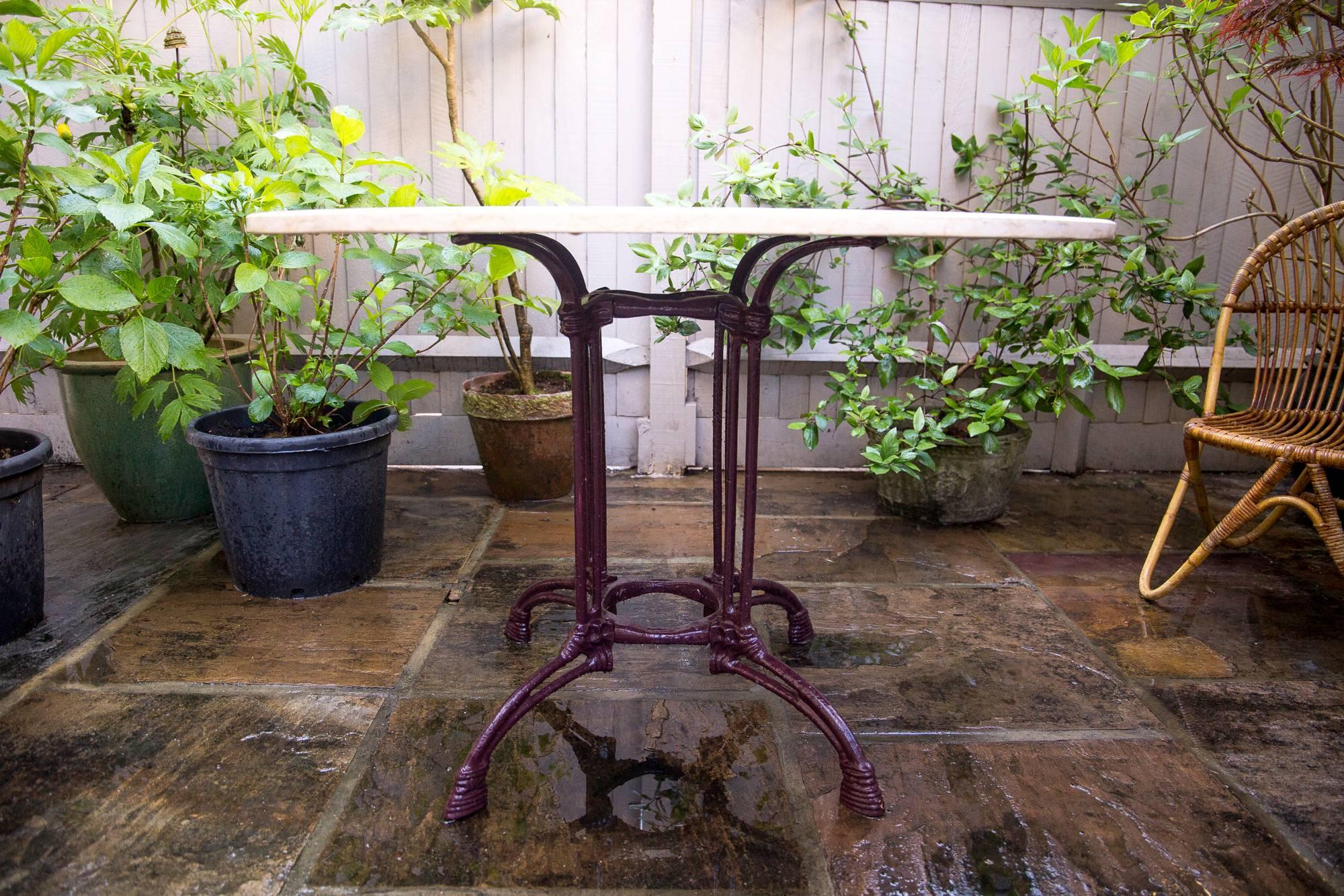 Featuring an elegant Art Nouveau wrought iron base, made of of four outward spayed straps for the table top, descending into four double columns and terminating in a rounded stretcher and four spayed hoof like feet - in dark claret colour. The top a