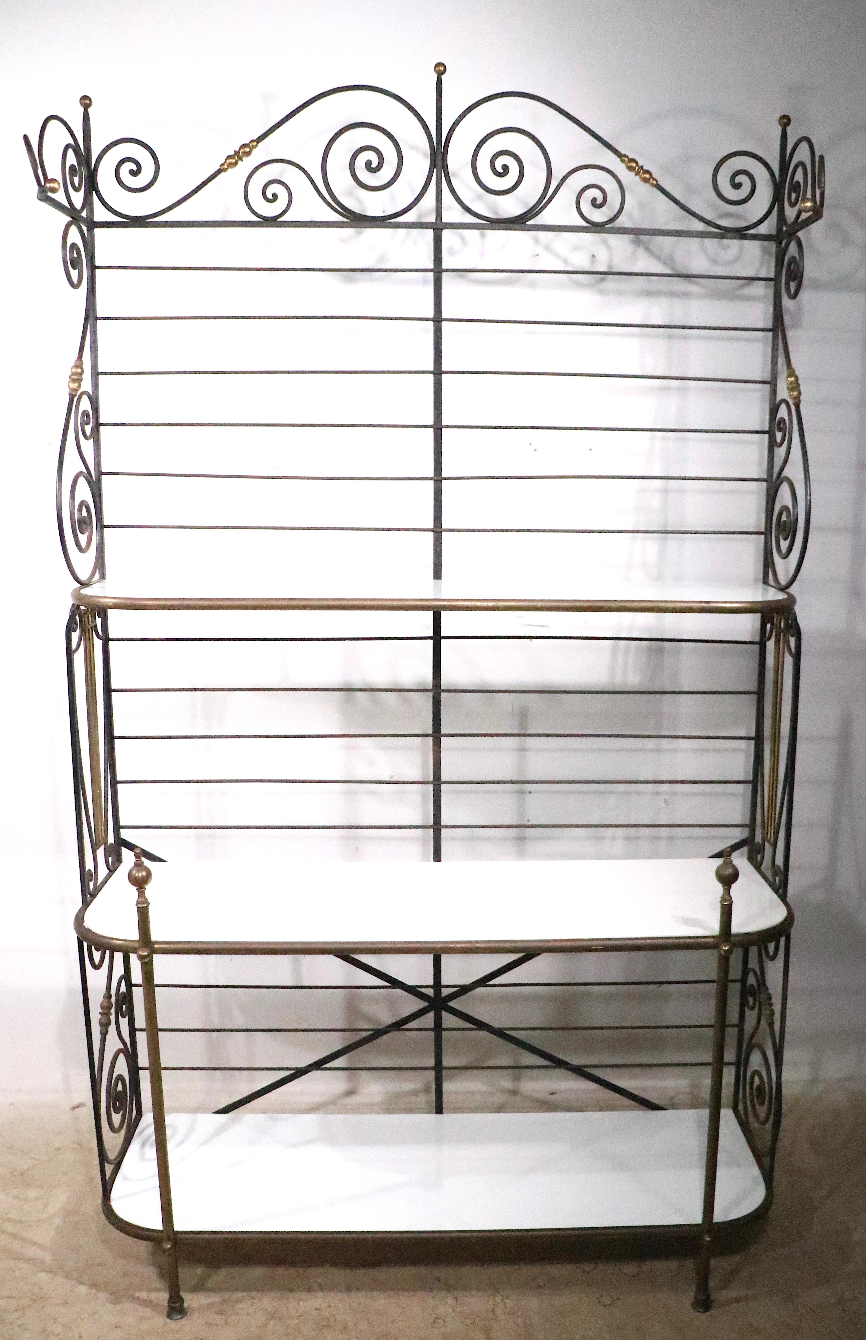 Impressive French Bakers Rack of wrought iron, brass, and white milk glass. The rack features three glass shelves of varied  depth, that fit into the decorative metal frame which is constructed of wrought iron with brass trim. 
 This is a 20th