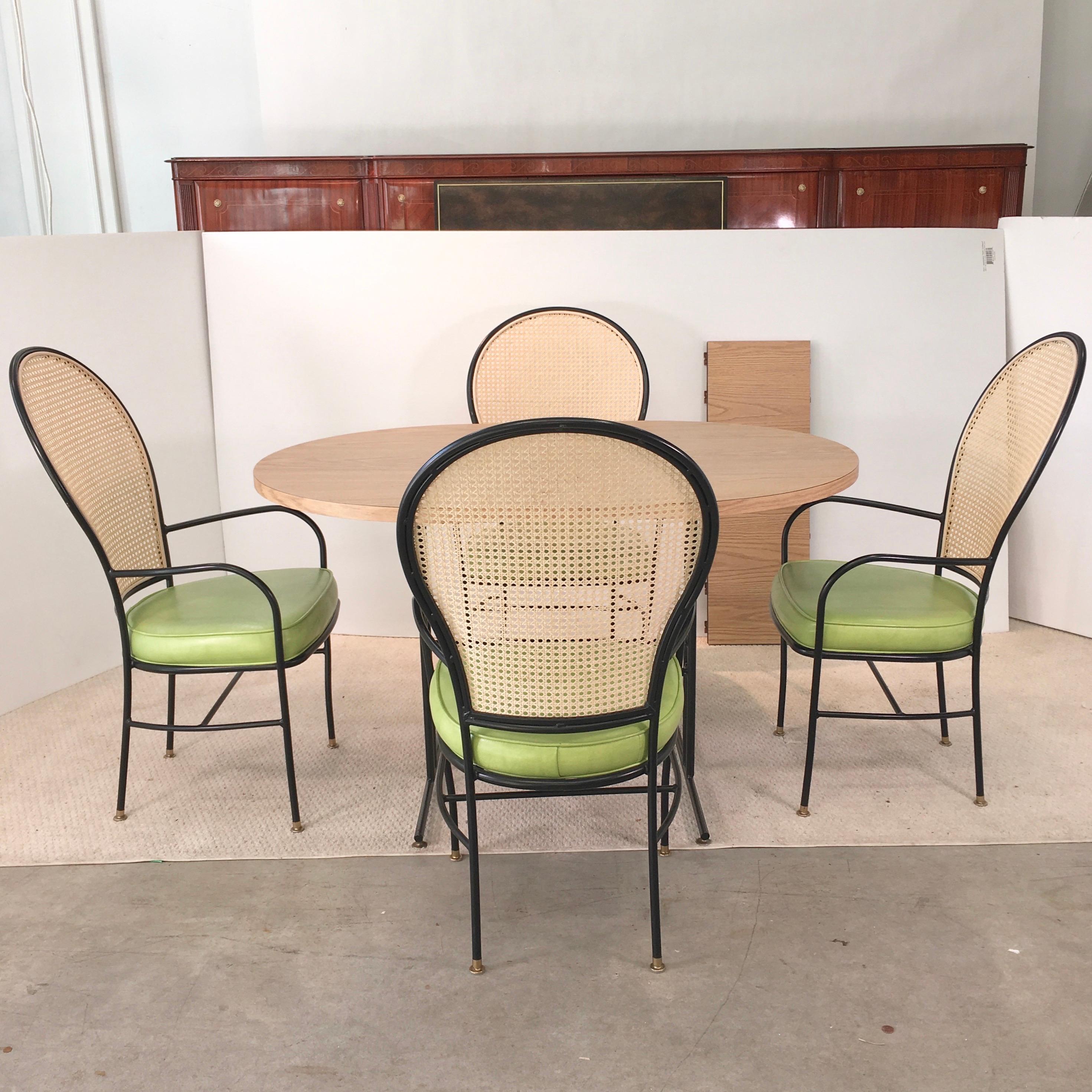 Vintage dinette with great silhouette iby Milo Baughman. Four newly re-caned balloon back blackened iron arm chairs with lime green naugahyde seat cushions and brass tone glide feet. Racetrack oval light oak woodgrain laminate table, expandable with