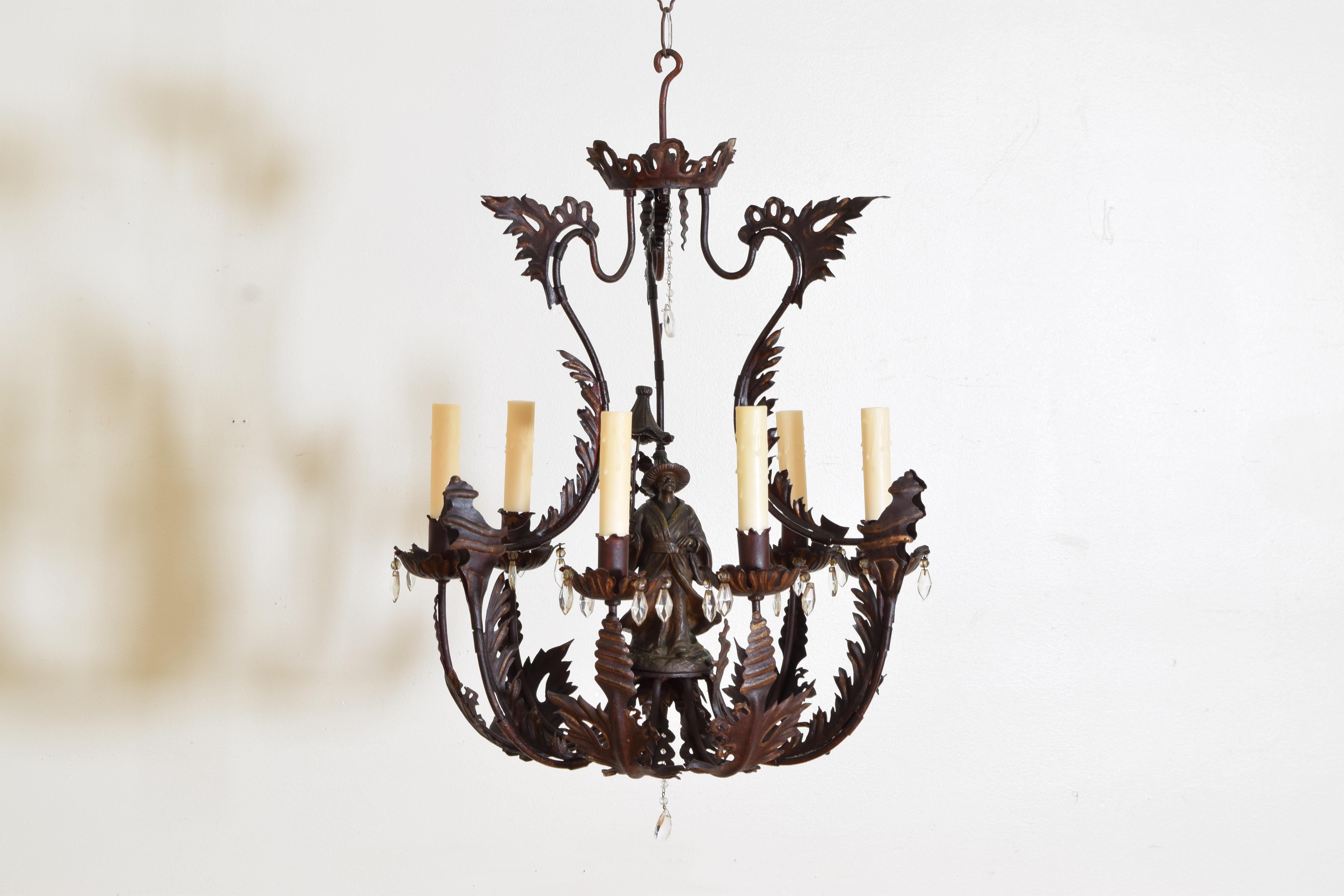 construit en fer forgé et en fonte, peint et doré, ce lustre présente un sommet en forme de pagode avec un cadre à volutes et des formes de feuilles attachées à un fond de panier. Au centre se trouve une figure chinoise en métal moulé tenant un