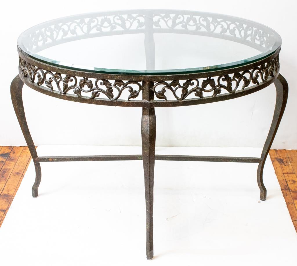 Wrought iron circular table with glass top above a floral openwork apron above cabriole legs joined by an X-stretcher. 

Dealer: S138XX