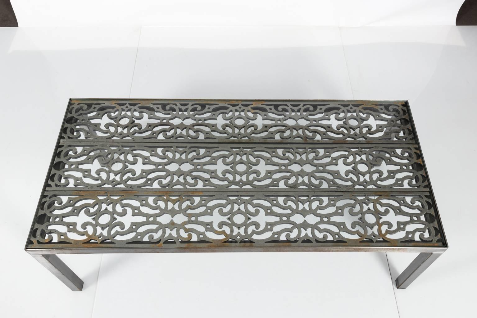 Contemporary wrought Iron coffee table that features a painted s-scroll wrought iron grate with a glass top. This piece also comes with some minor weathered patina.
 