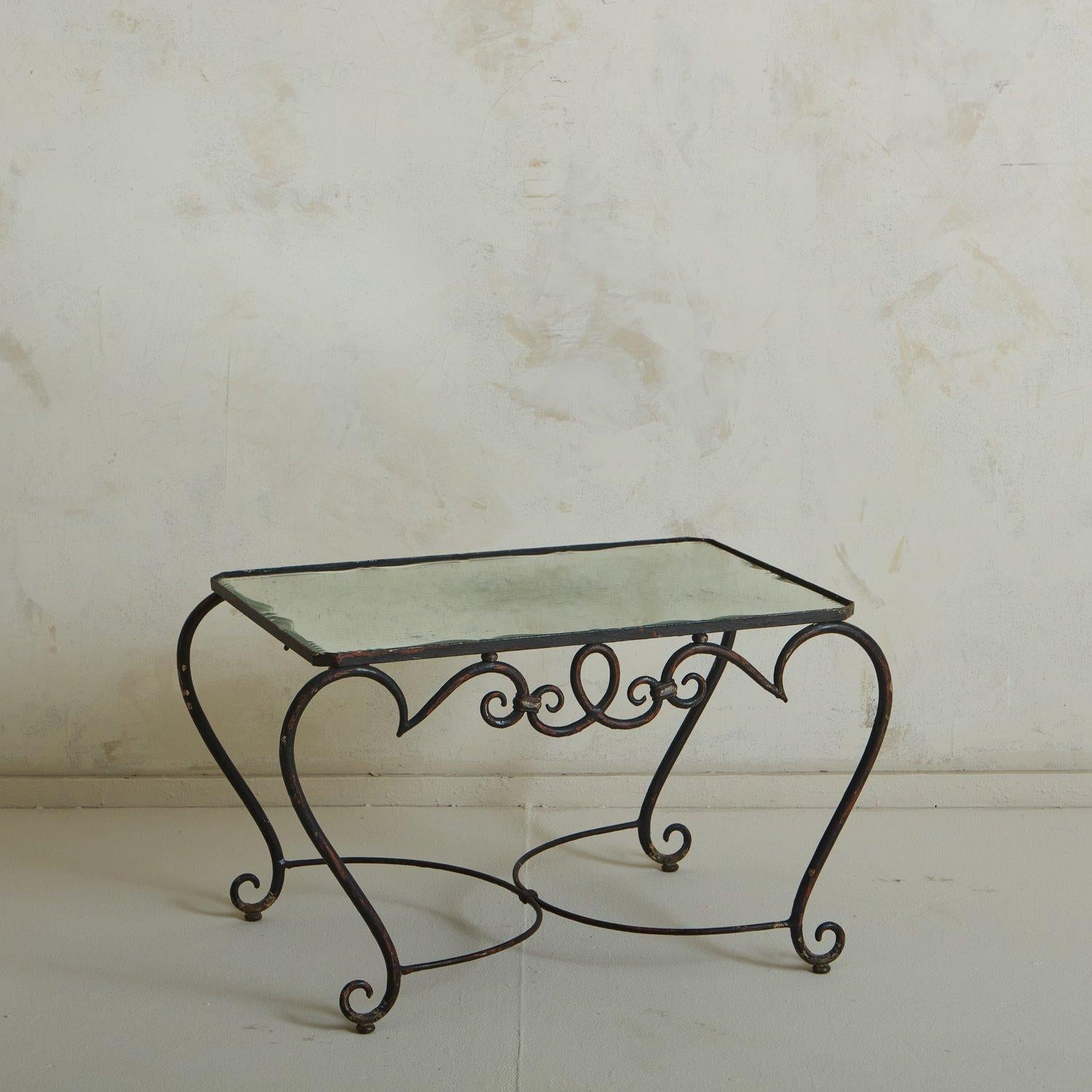 A 1940s French coffee table in the style of Rene Prou. This table features a wrought iron base with dramatically curved legs and curl details. It has an inset mirrored glass tabletop. Sourced in France, 1940s.