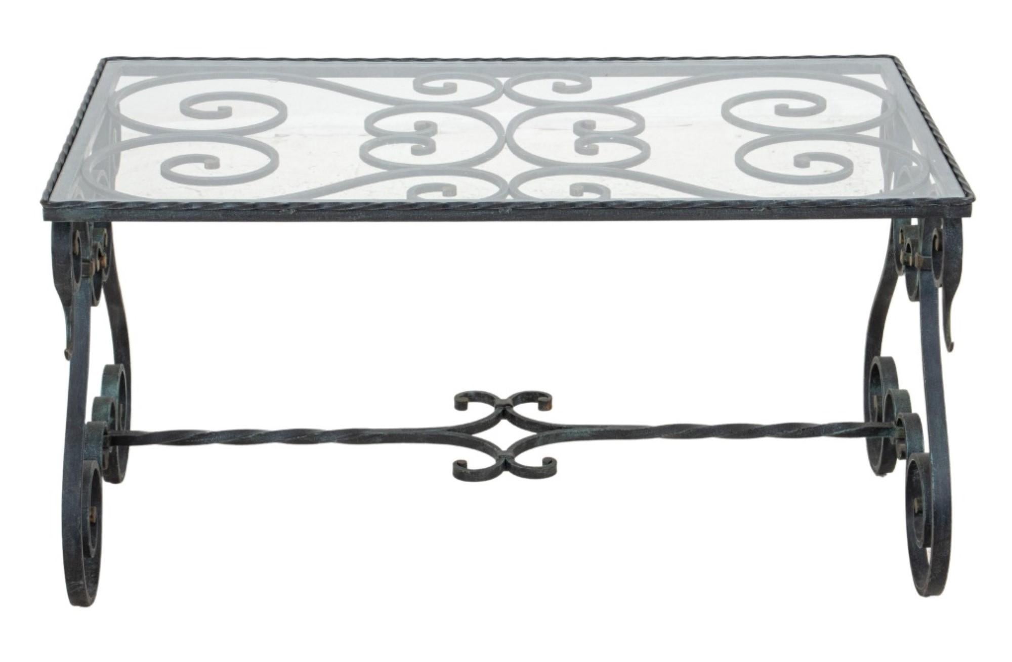 Wrought iron low table or coffee table with scrolled stretcher-joined legs and a glass top.

18 inches in height, 36 inches in width, and 20.5 inches in depth.
