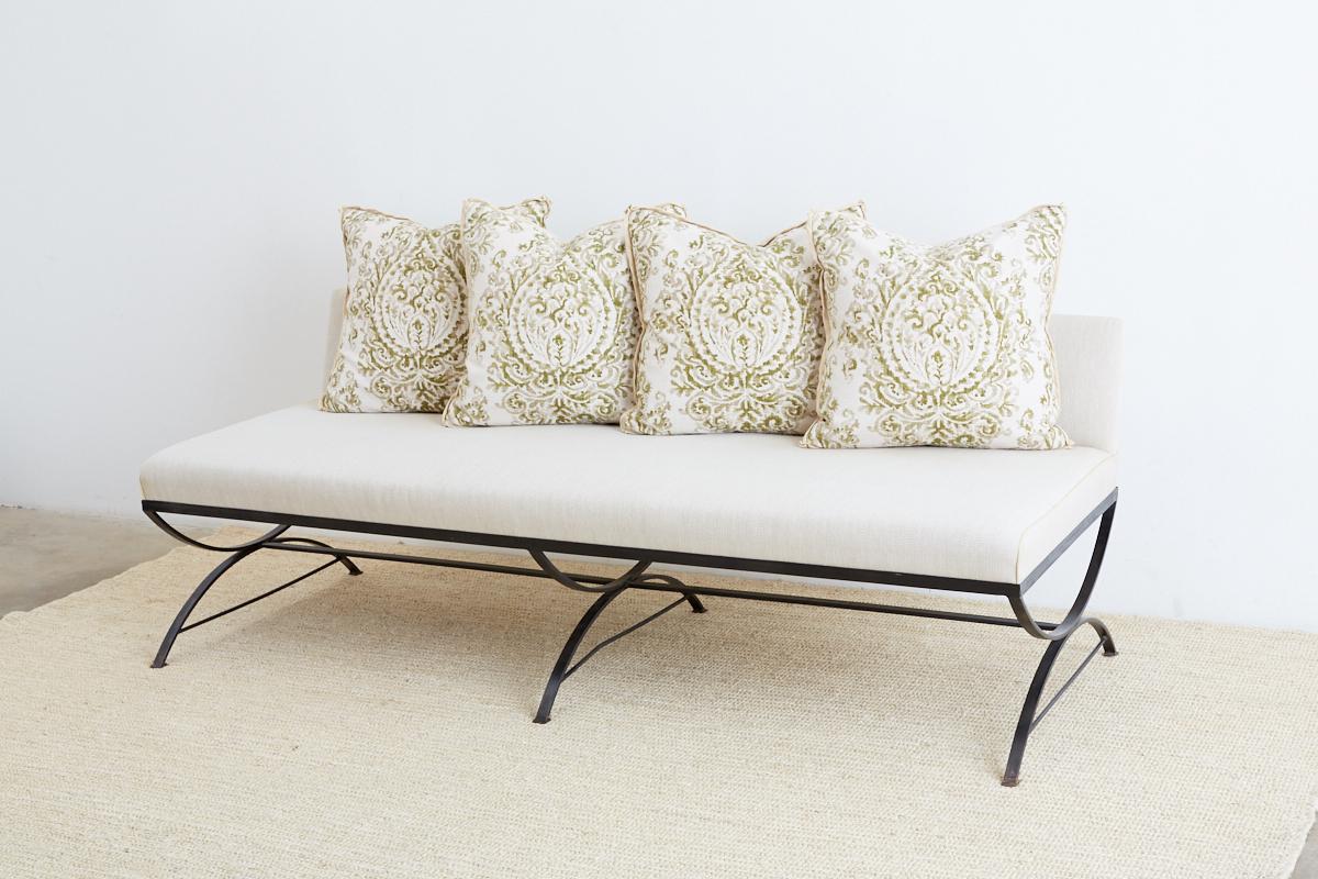 Chic wrought iron dining banquette bench or sofa featuring a Curule style base. The low back bench is upholstered and has six decorative pillows (2 large, 4 medium) with an organic textured linen fabric in a botanical style palmette design.