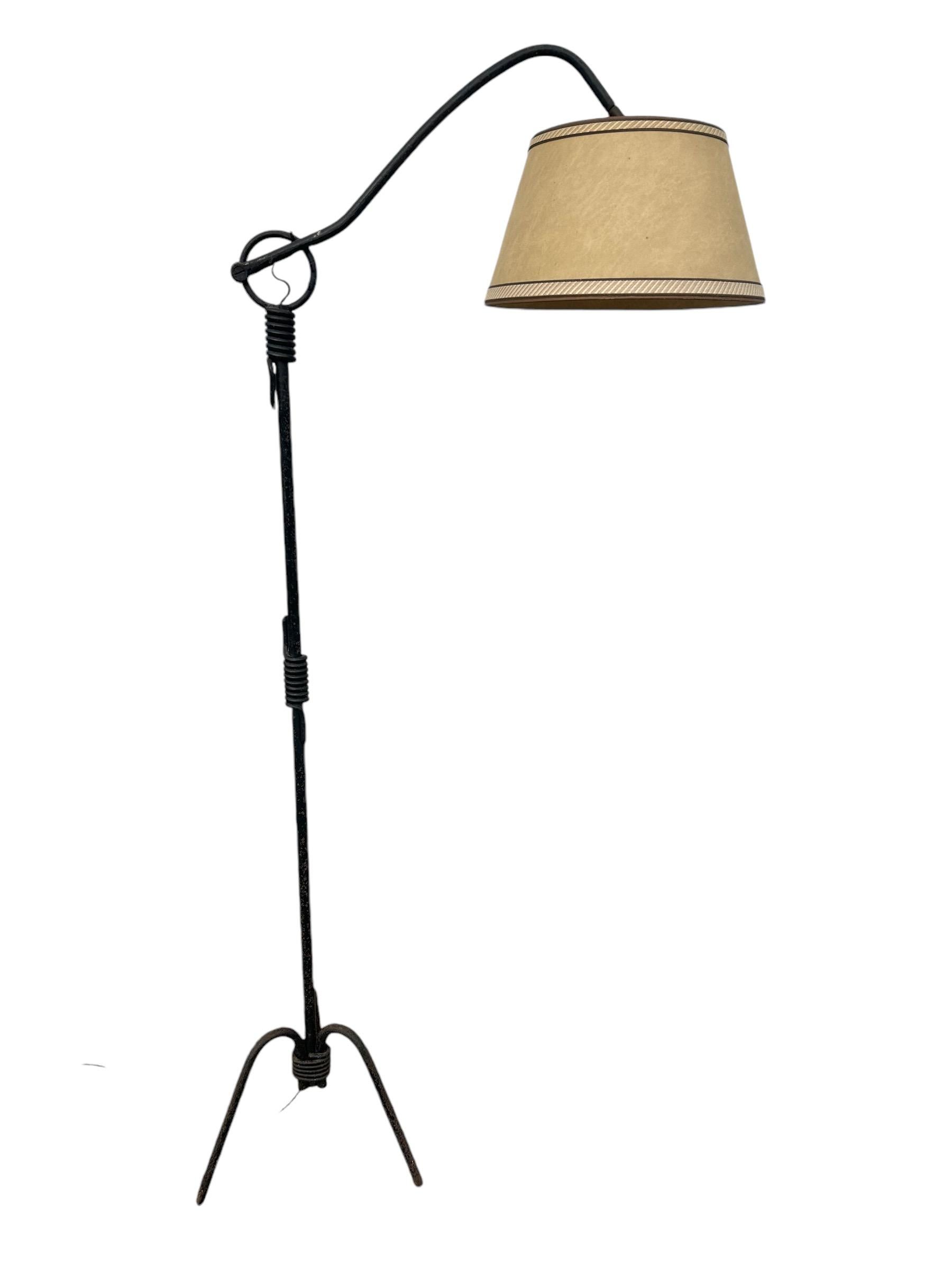 Elegant lampadaire tripode moderniste français en fer forgé avec bras articulé sur crémaillère pour monter ou descendre l'abat-jour, conçu dans les années 1950. La lampe est dans son état d'origine et conserve son abat-jour d'origine.

Cette lampe a