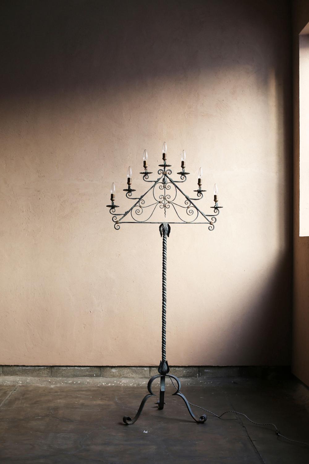 Esta lámpara de pie vintage se fabricó en Francia.
Su estructura de hierro forjado a mano presenta elementos decorativos de hierro forjado, como giros y volutas.
La barra de soporte que sale de la base del trípode está retorcida en espiral, y el