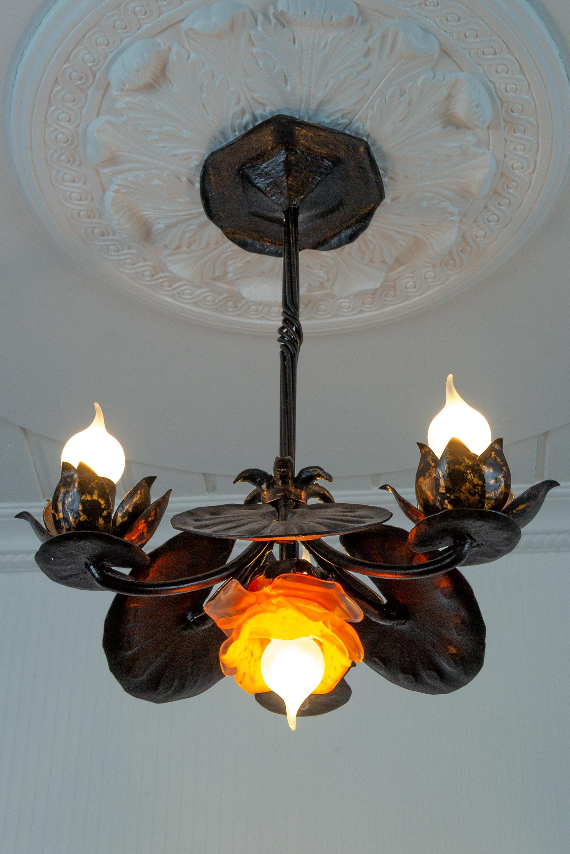 Adorable wrought iron chandelier with three points of light directed upwards in the shape of a water lily, petals decorated with red gold color patina. Bobeches are small stylized water lily pads. A beautiful flower-shaped lampshade made of orange