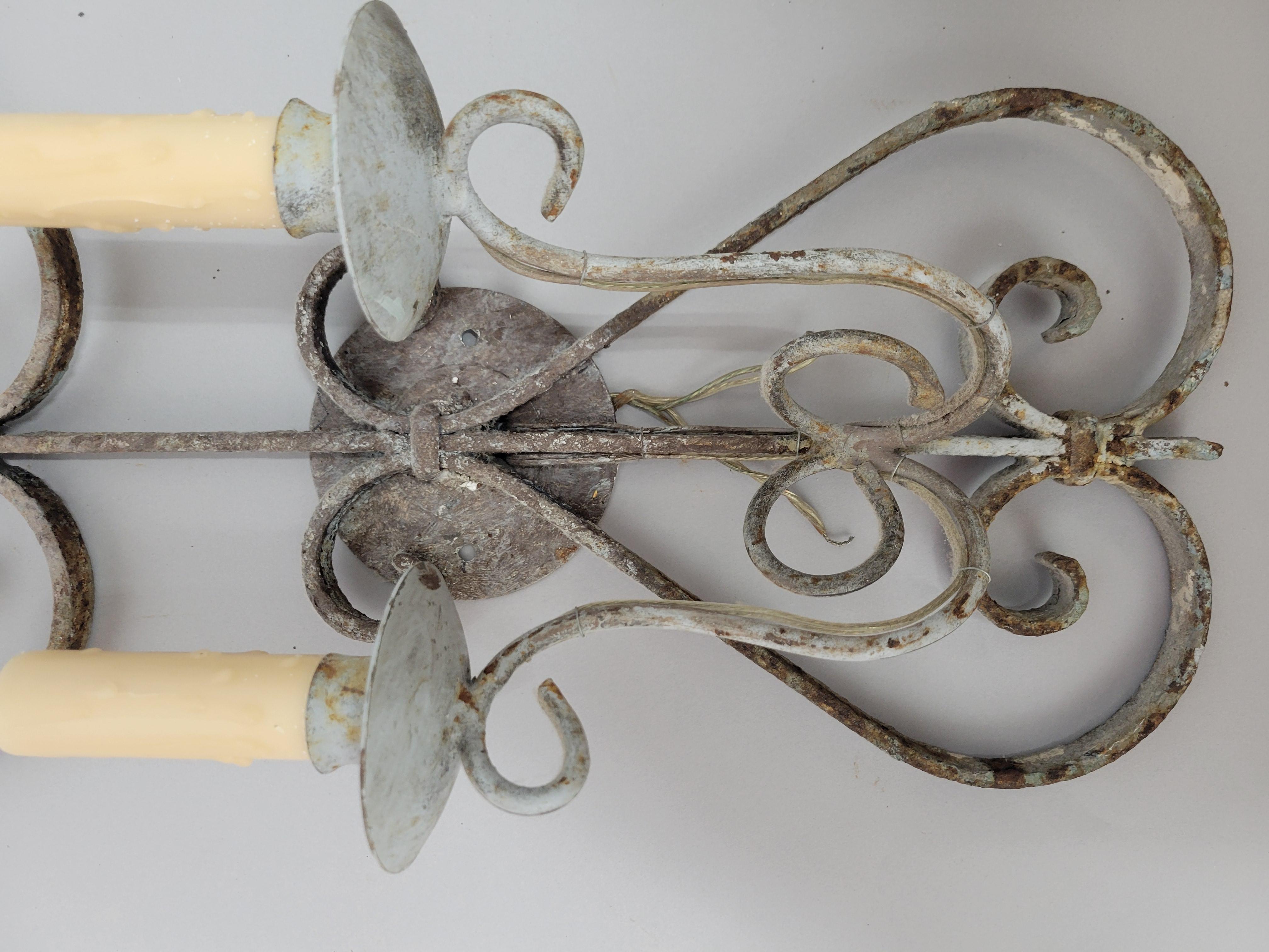 Eleva la decoración de tu hogar con este exquisito par de apliques antiguos de hierro forjado. Estas piezas intemporales presentan un intrincado trabajo de volutas y una hermosa pátina que sólo se consigue con el paso del tiempo. Cada candelabro ha