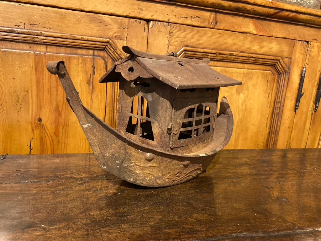 Charming and whimsical iron hanging lantern in the form of a the Chinese sailing vessels known as junks. The hull decorated with raised waves and round bosses, the cabin with a hinged door that opens so a candle can be placed inside. An iron ring on