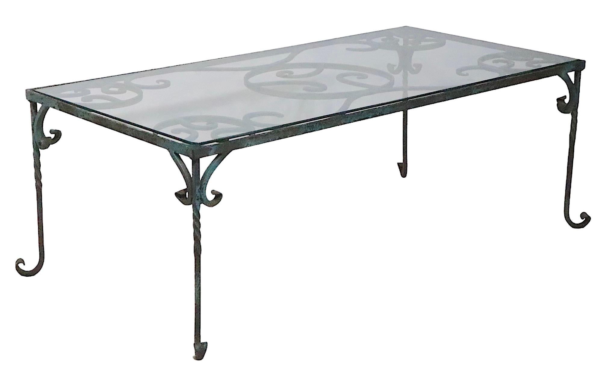 Exquisite wrought iron coffee table in original patinated old paint surface. The table features a decorative scroll work top, and delicate curled iron feet. It is hard to find the coffee table form, and this one is exceptional. The glass top shown