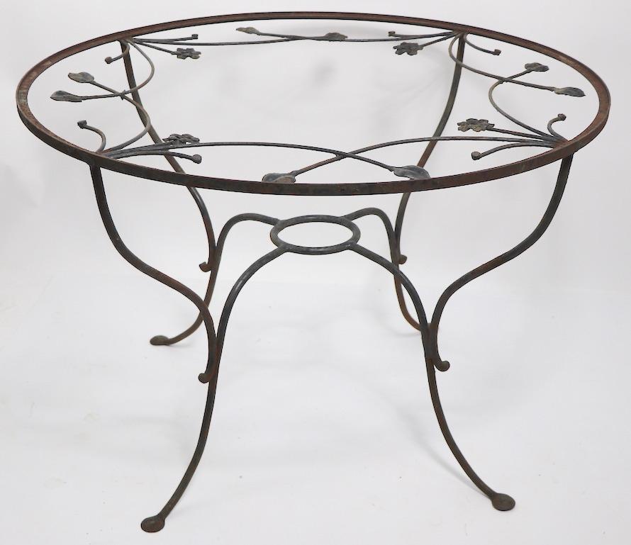 Charming and elegant wrought iron garden, patio table attributed to Salterini. Circular top with decorative floral foliate interior metal work, arched stretcher with a ring form center element to accept a potted plant if you like. Currently in old