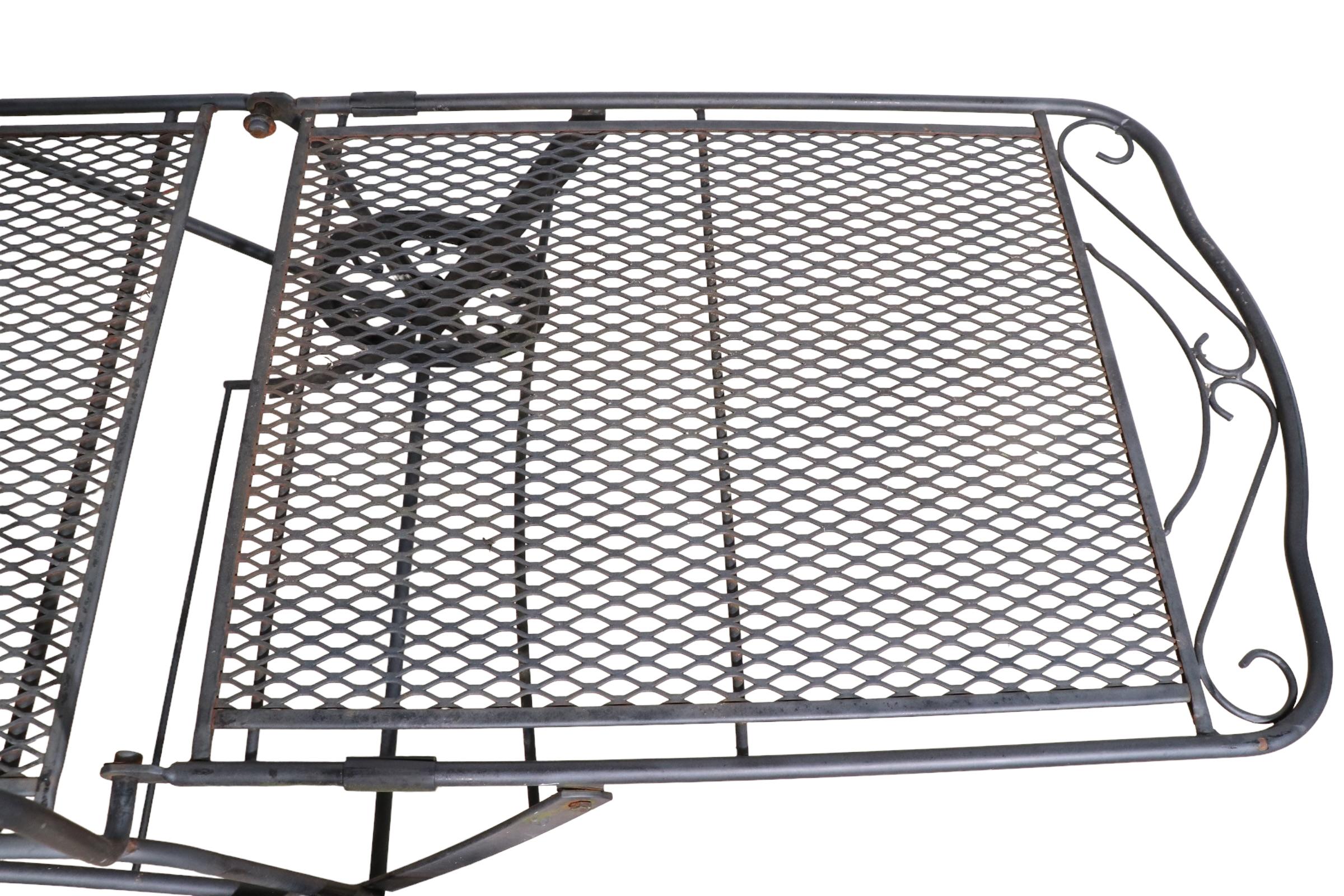 Stylish wrought iron and metal mesh adjustable chaise lounge attributed to the Woodard Furniture Company. The chaise has a reclining backrest, and wheels to easily move the piece. Perfect for poolside, patio, or garden use, suitable for both indoor