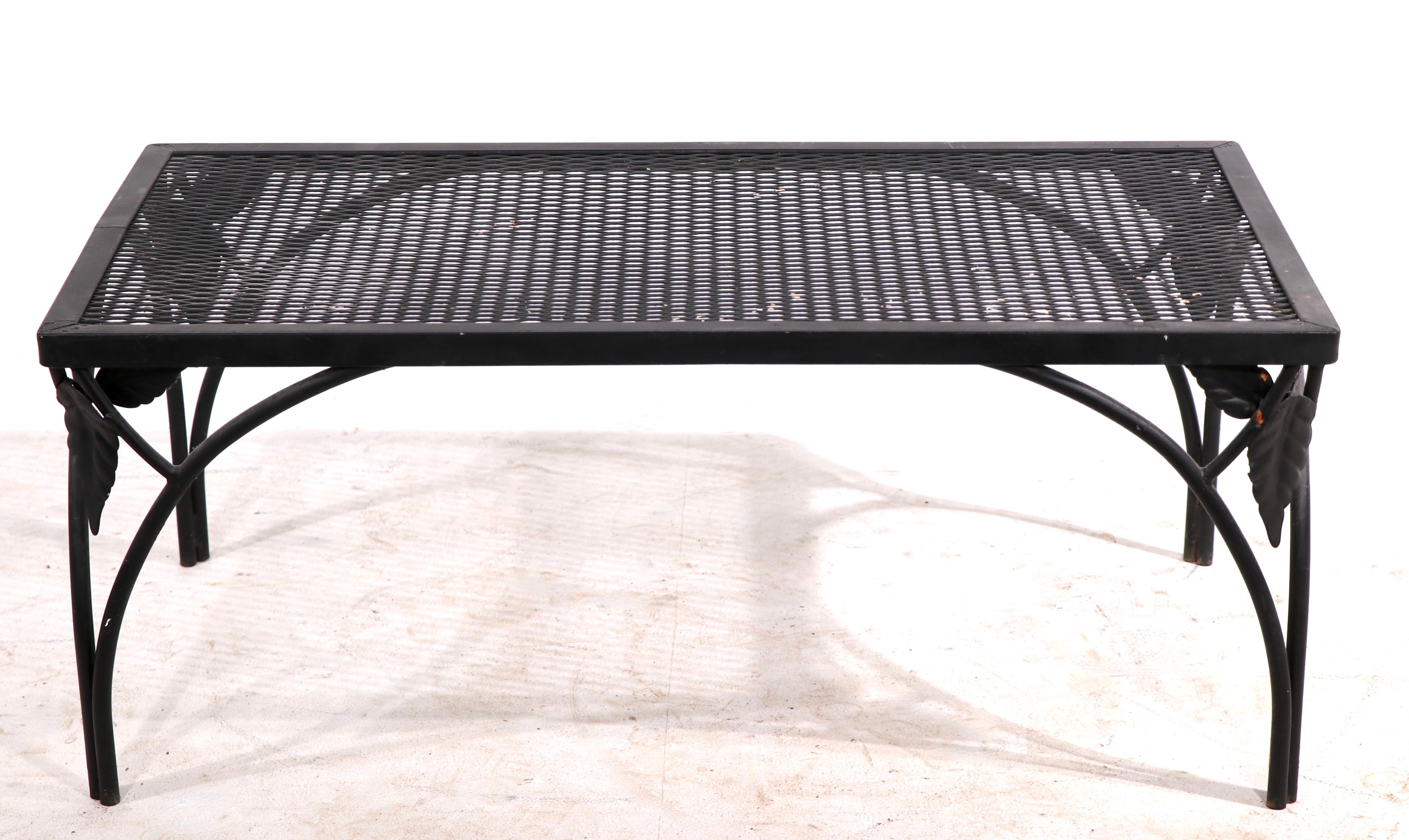 Unusual wrought iron coffee table having a metal mesh top with arched iron legs and decorative metal leaves at the corners. The table is structurally sound and sturdy, showing only light cosmetic wear, normal and consistent with age. Currently in