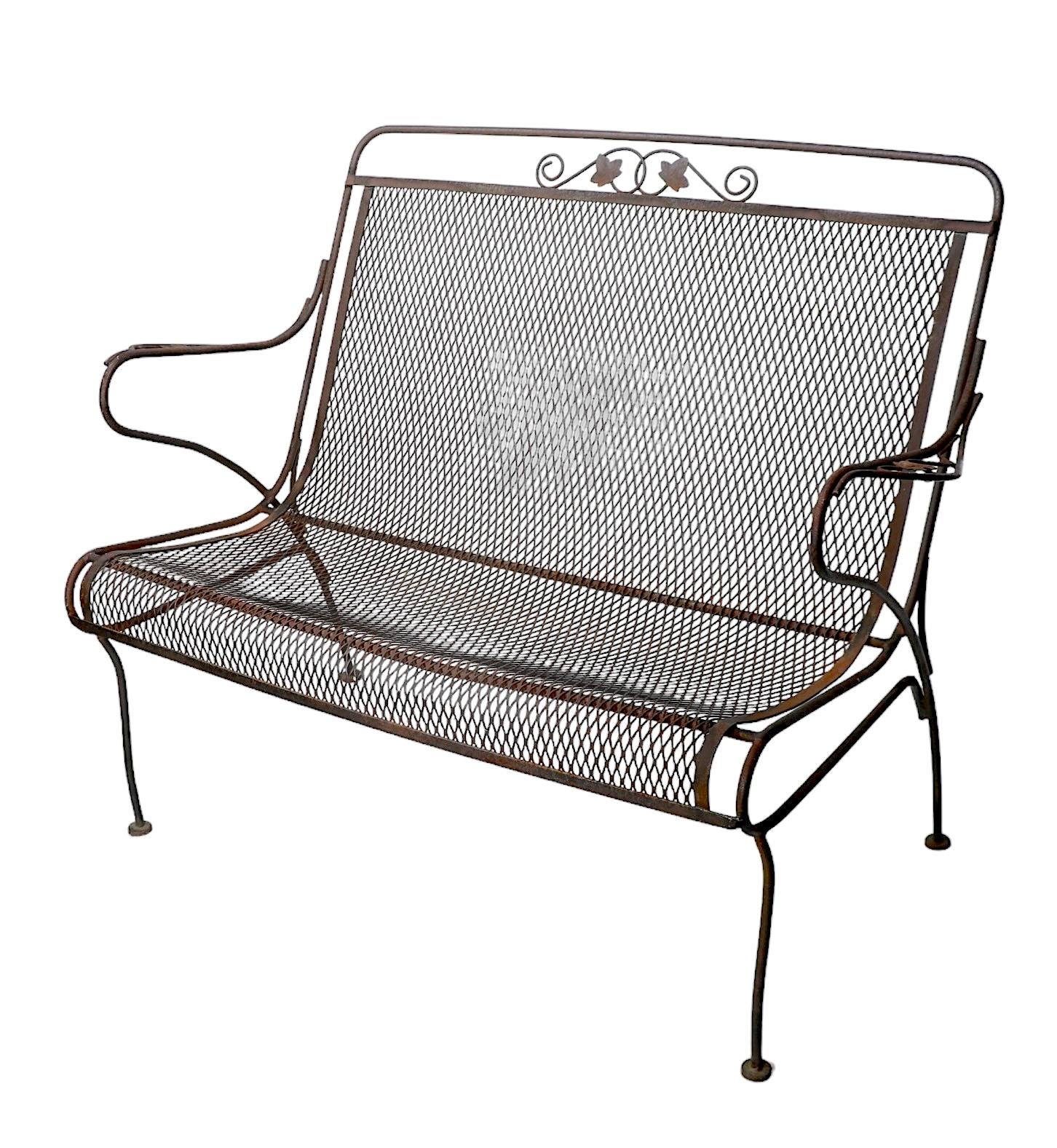 Classic vintage garden, patio, poolside, bench, attributed to Salterini, or possibly Woodard. The loveseat features a wrought iron frame with a continuous seat and backrest made of metal mesh. This example is structurally sound and sturdy, showing