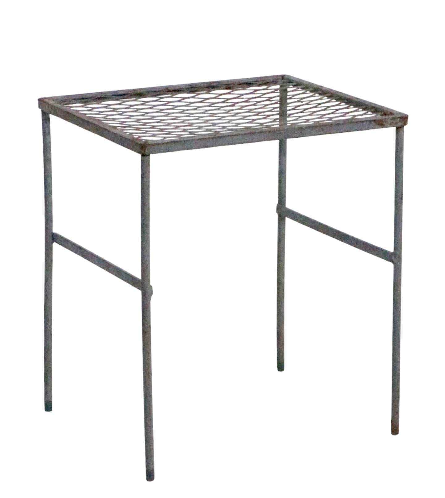 Architectural side, end table having a wrought iron base, with a metal mesh top. The table is in very good original condition, clean and ready to use, it is in grey paint finish. Manufacture attributed to Salterini, in the style of Woodard.