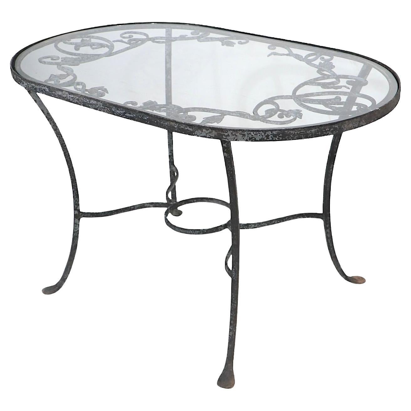 Tavolino chic da giardino, patio e piscina in ferro battuto di Salterini. Questo piccolo tavolo è caratterizzato da un  La struttura è in ferro battuto lavorato in modo intricato con decorazioni in metallo a fogliame e il piano originale in vetro