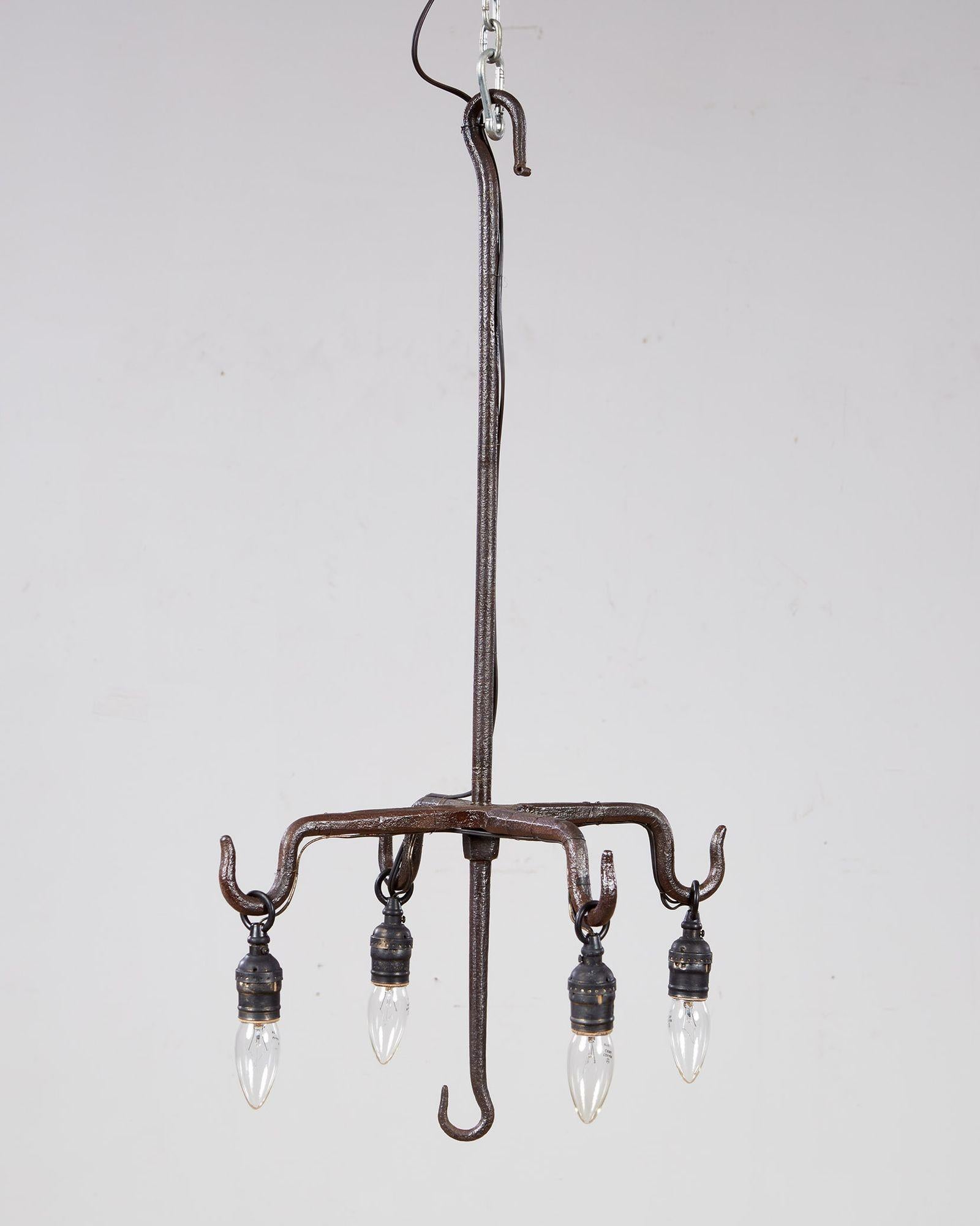 Un lampadario in ferro battuto nero con quattro bracci radiali e ganci integrati su uno stelo centrale anch'esso con ganci in alto e in basso.  Ora è cablato con prese a goccia per lampadine Edison.  Inghilterra, XIX secolo.  Dona un'atmosfera