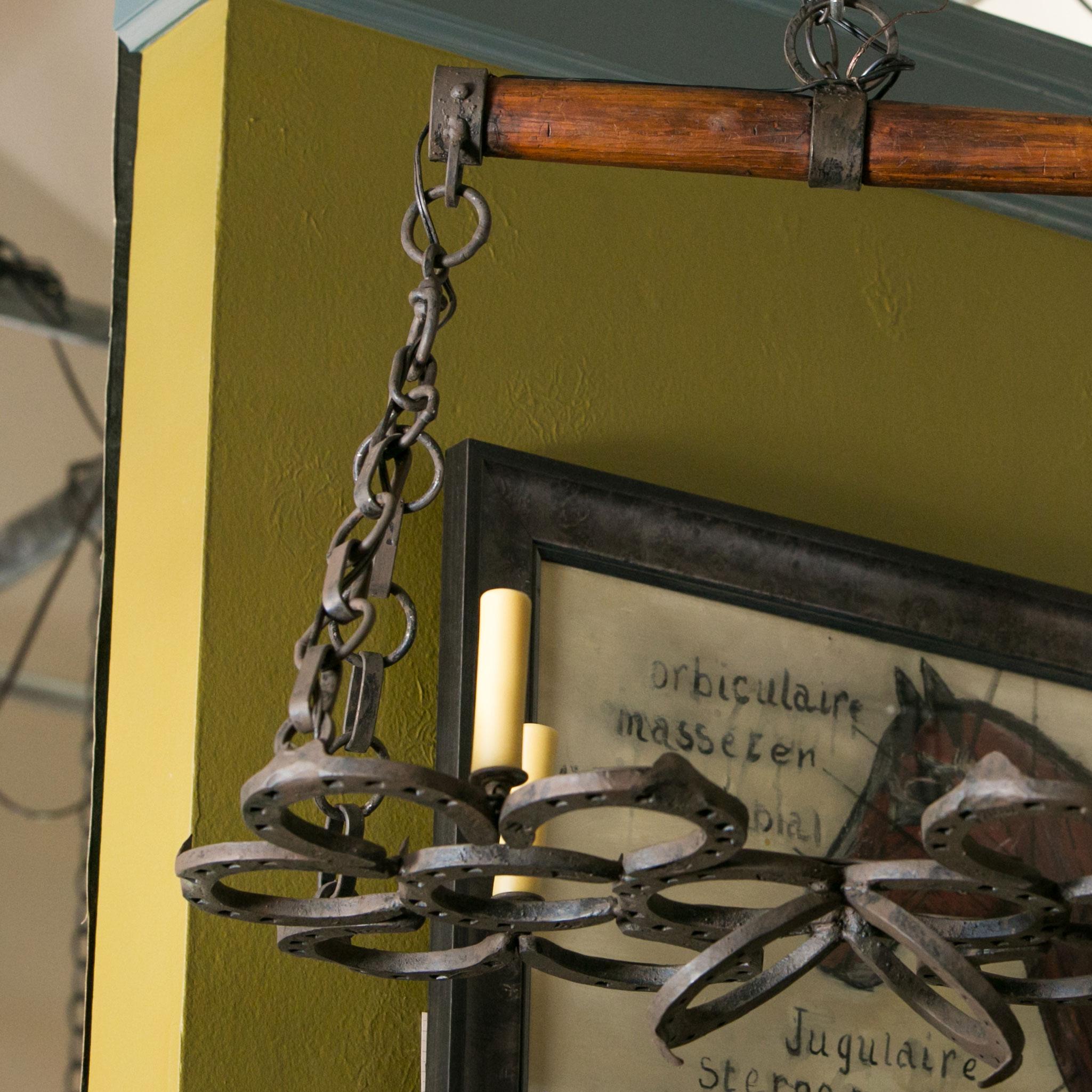 Wrought iron horseshoe chandelier. This rustic French light is completely handmade of 19th century hand-forged horseshoes. Similarly, the wooden beam at the top of the light is part of an antique yoke. Its chain is hand-forged. This equestrian-theme