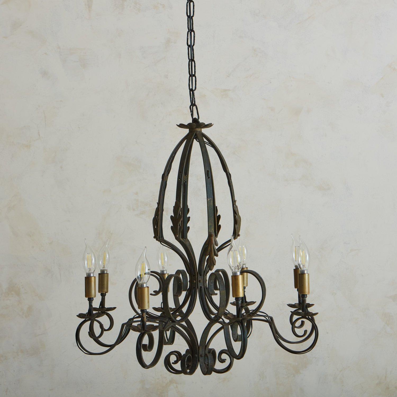 A 1920s French patinated iron chandelier with curved detailing. This chandelier has eight scalloped bobeches and new antiqued brass socket covers, which hold candelabra light bulbs. It hangs from a new chain and canopy. We love the scale of this