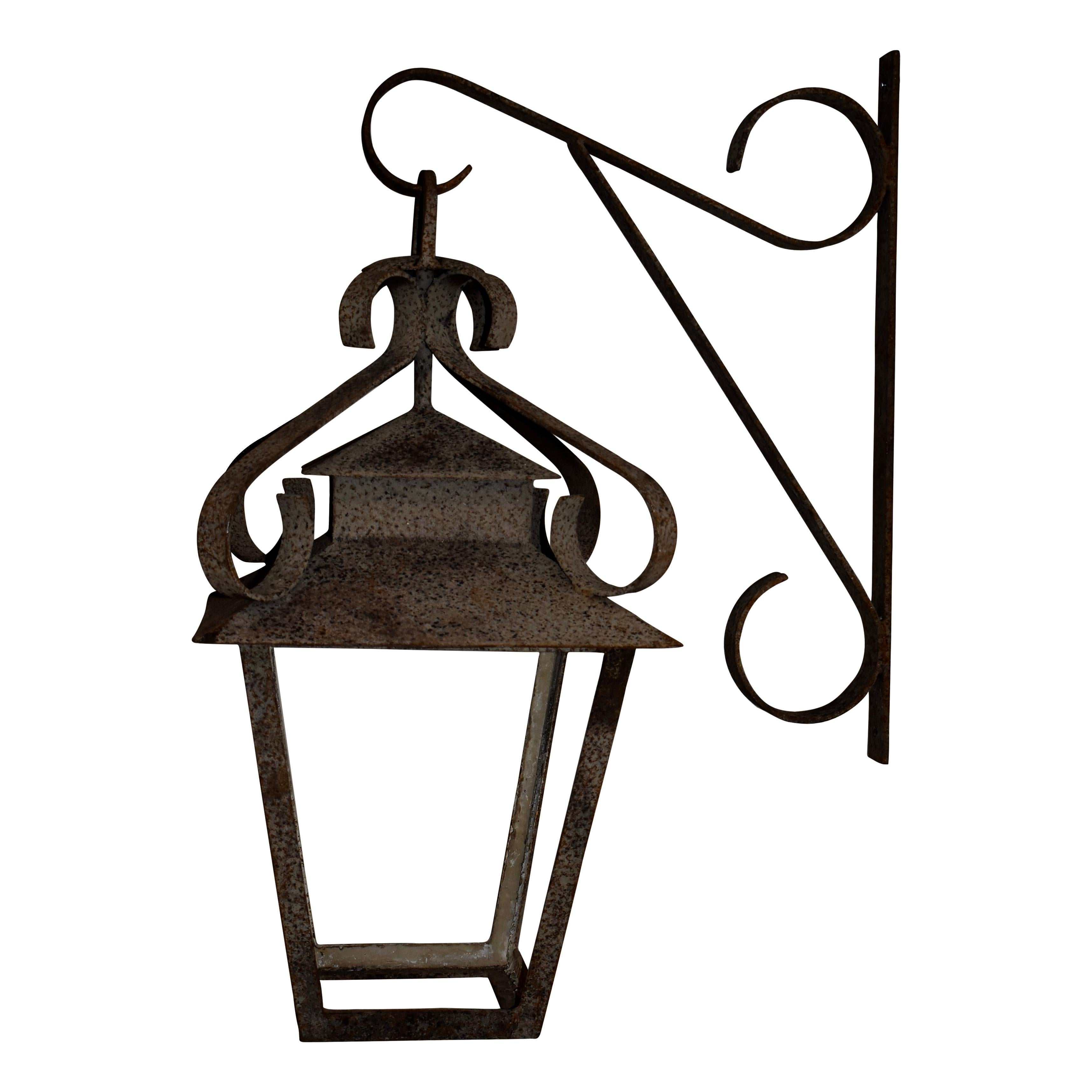 Suspended from a scrolled bracket, this wrought iron lantern features four tapered sides beneath a covered roof. Additional scrollwork over the roof adds simple elegance. No wiring. No glass.

Dimensions of lantern: 16.75