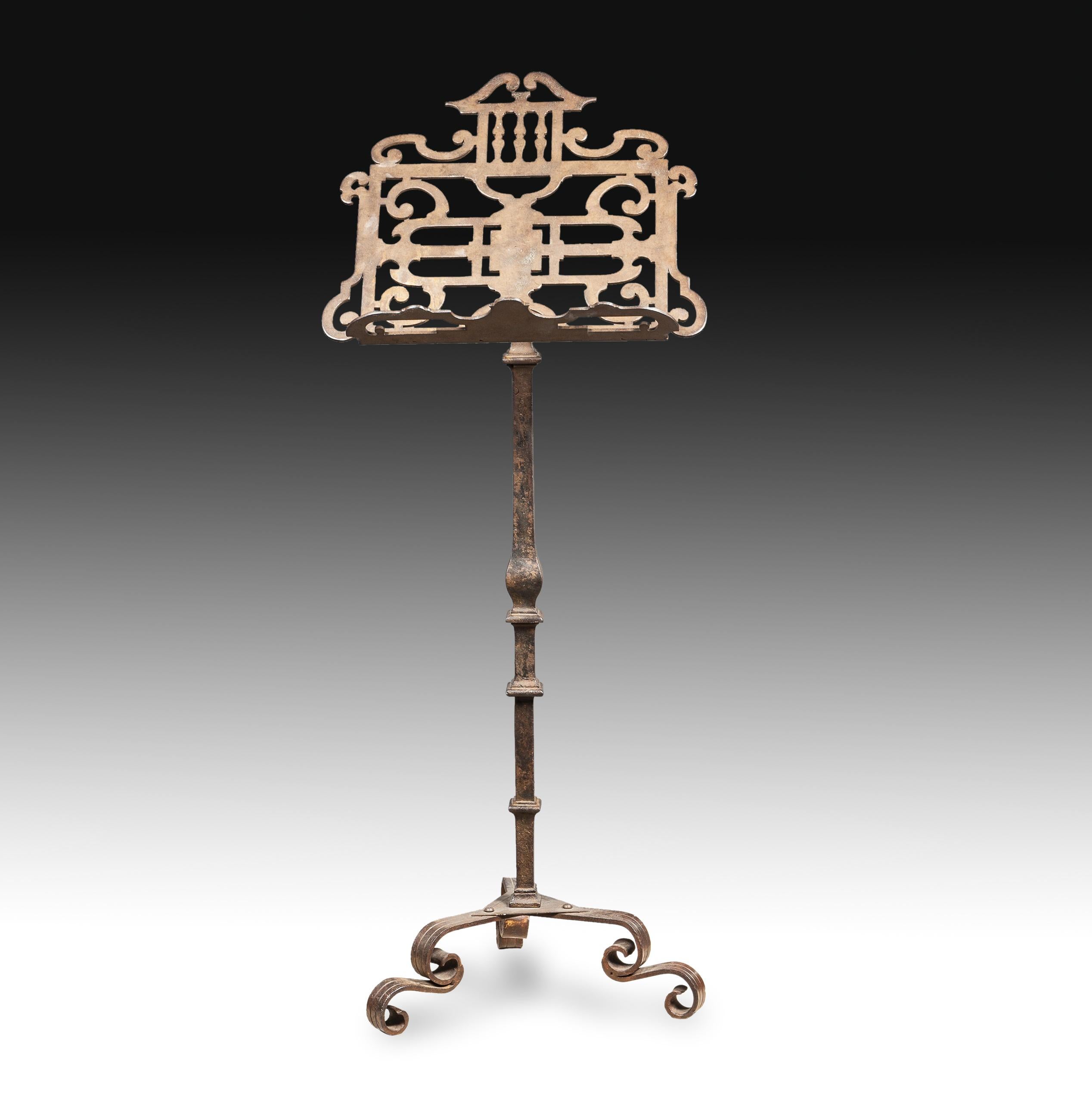 On three legs with scrolls stands a foot decorated with bulging forms and a flame towards the center, which holds and raises the lectern, which stands out for its architectural elements and simplified vegetables inspired by classical antiquity. The
