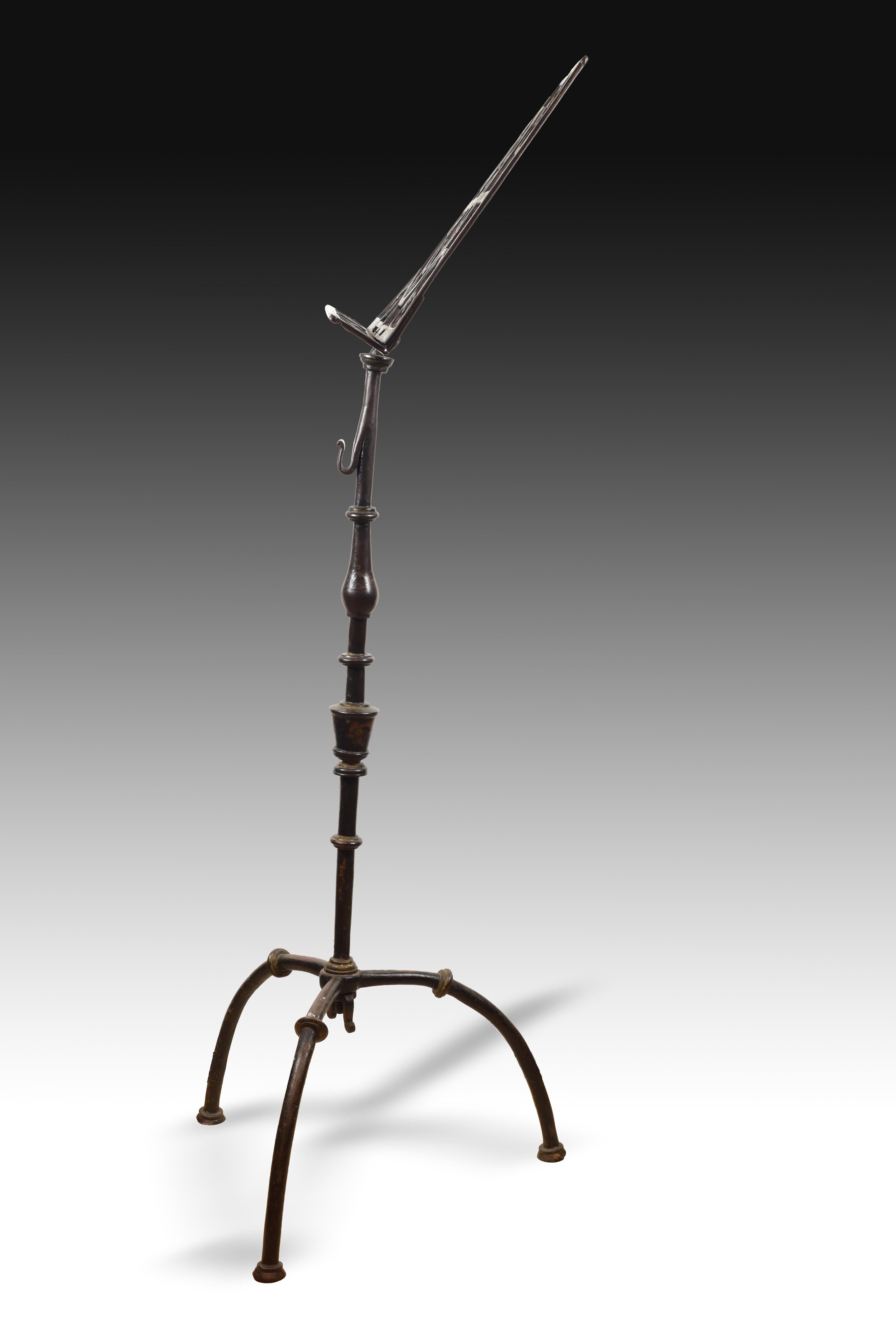 On a tripod with curved legs decorated with a disc in the center, stands the piece, also decorated with those same discs and, in addition, with a central vase and a baluster on the top. The lectern that finishes is decorated by heart-shaped iron