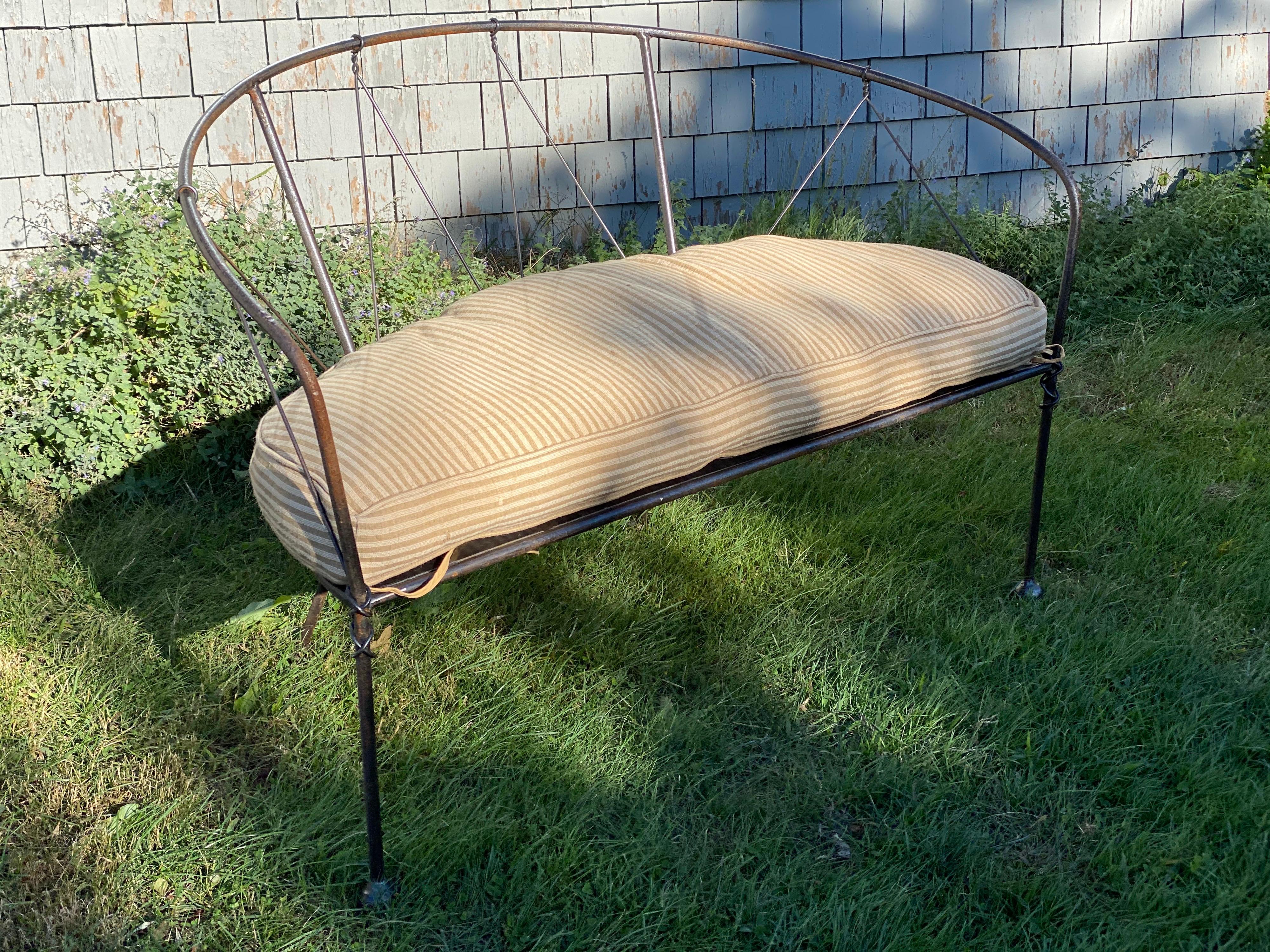 Wrought iron loveseat or settee is handcrafted. Great for indoor use and outdoor with treatment. Striped cushion custom made for seat. Lightly used. Slight rust color coming through in some spots. Iron slats seat like a basket weave