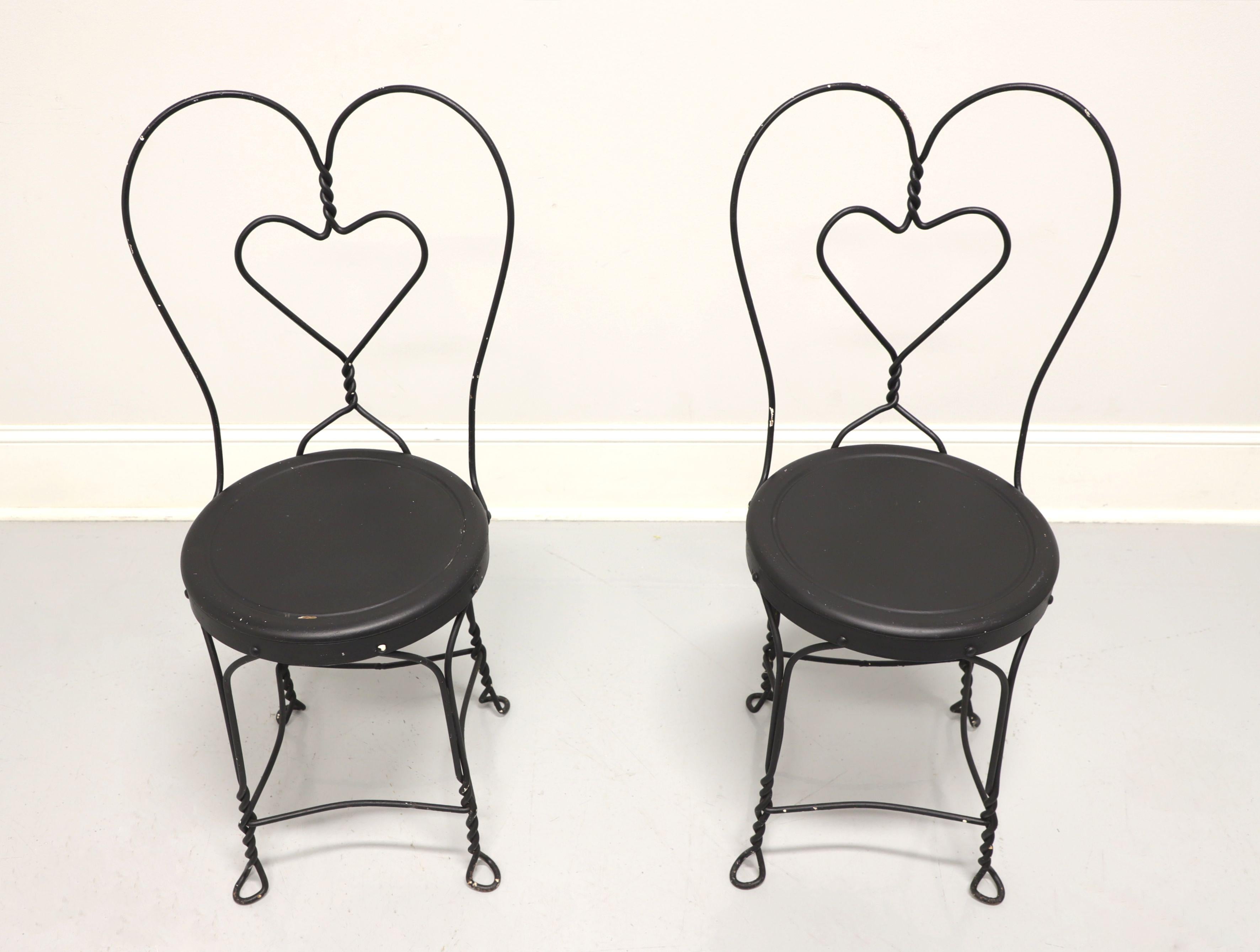 A pair of Victorian style wrought iron ice cream parlor bistro chairs, unbranded. Wrought iron metal frames, distressed black painted finish, metal seats, twisted backs and legs. Ready for a fresh coat of paint or can be used as-found. Made in the