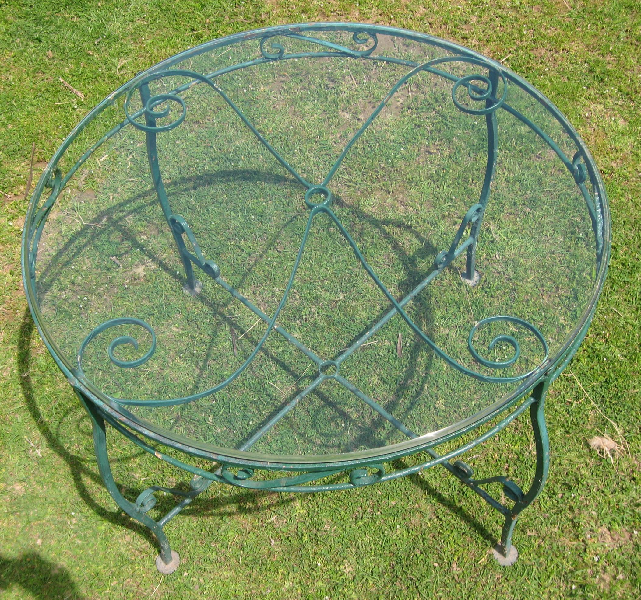 Five-piece wrought iron dining / patio set. One glass-topped table and four chairs. Painted green. Table measures:
42.5 in across.- 29-3/8 in high. - 29- 11/16 in high. With glass top. Chairs measure: 33.5 in high x 17.25 in wide x 22.5 in deep.