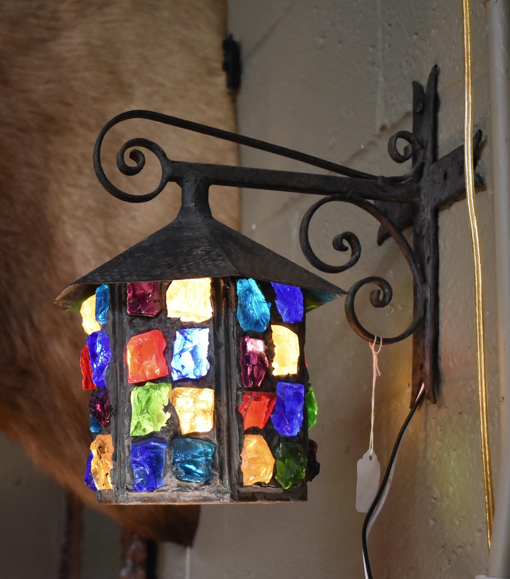 Single socket Tudor iron and multicolored chunk glass lantern by English designer Peter Marsh. Wrought iron bracket supports sconce. Cross form wall mount. Bracket arm protrudes 9