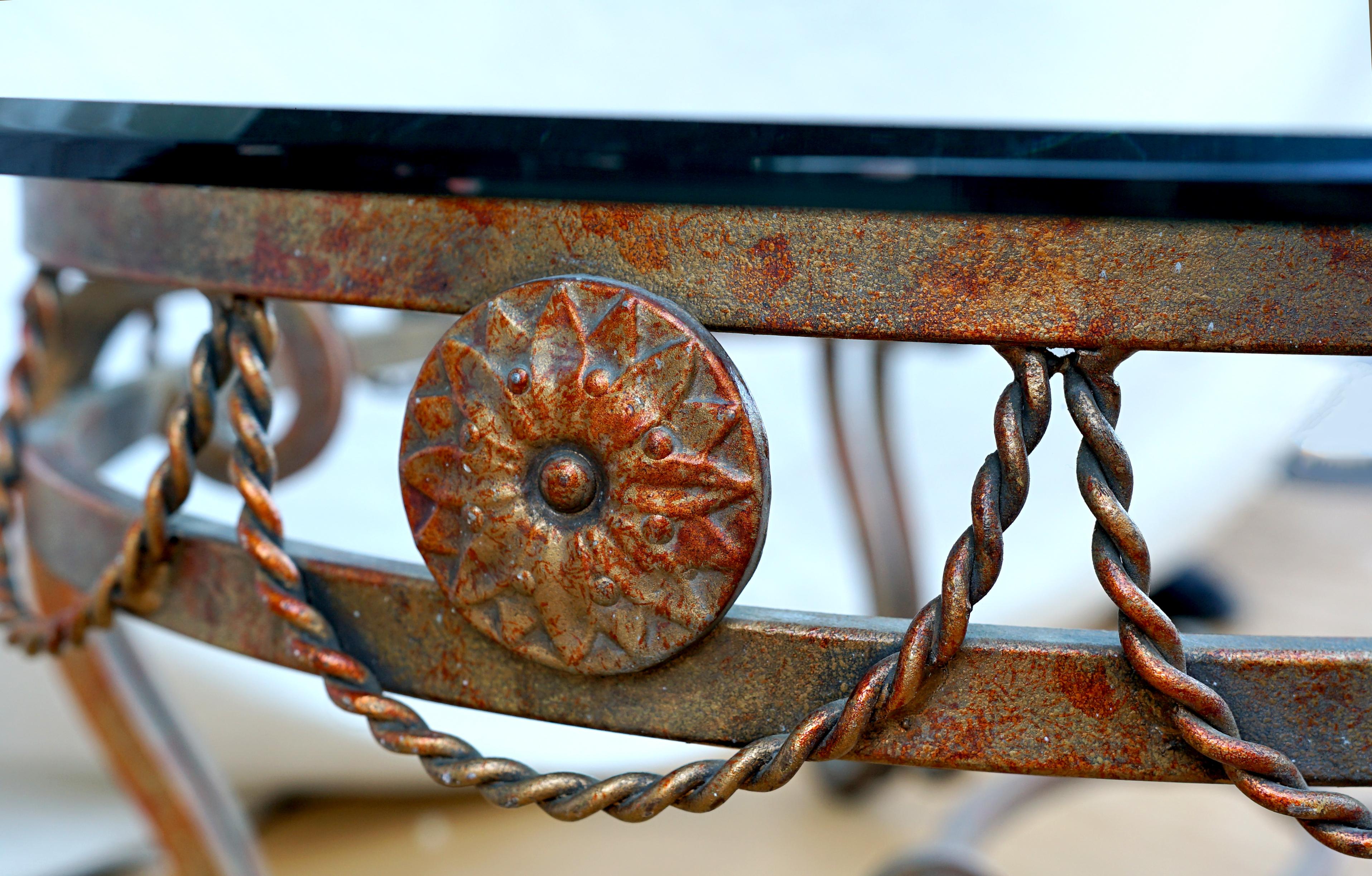 Scrolls and wrought iron swag ropes make this table a standout. The detailing and craftsmanship in iron is attractive. 
OF oval section with beveled glass top, the frame with scrolled and interlocking elements, twisted swag 
