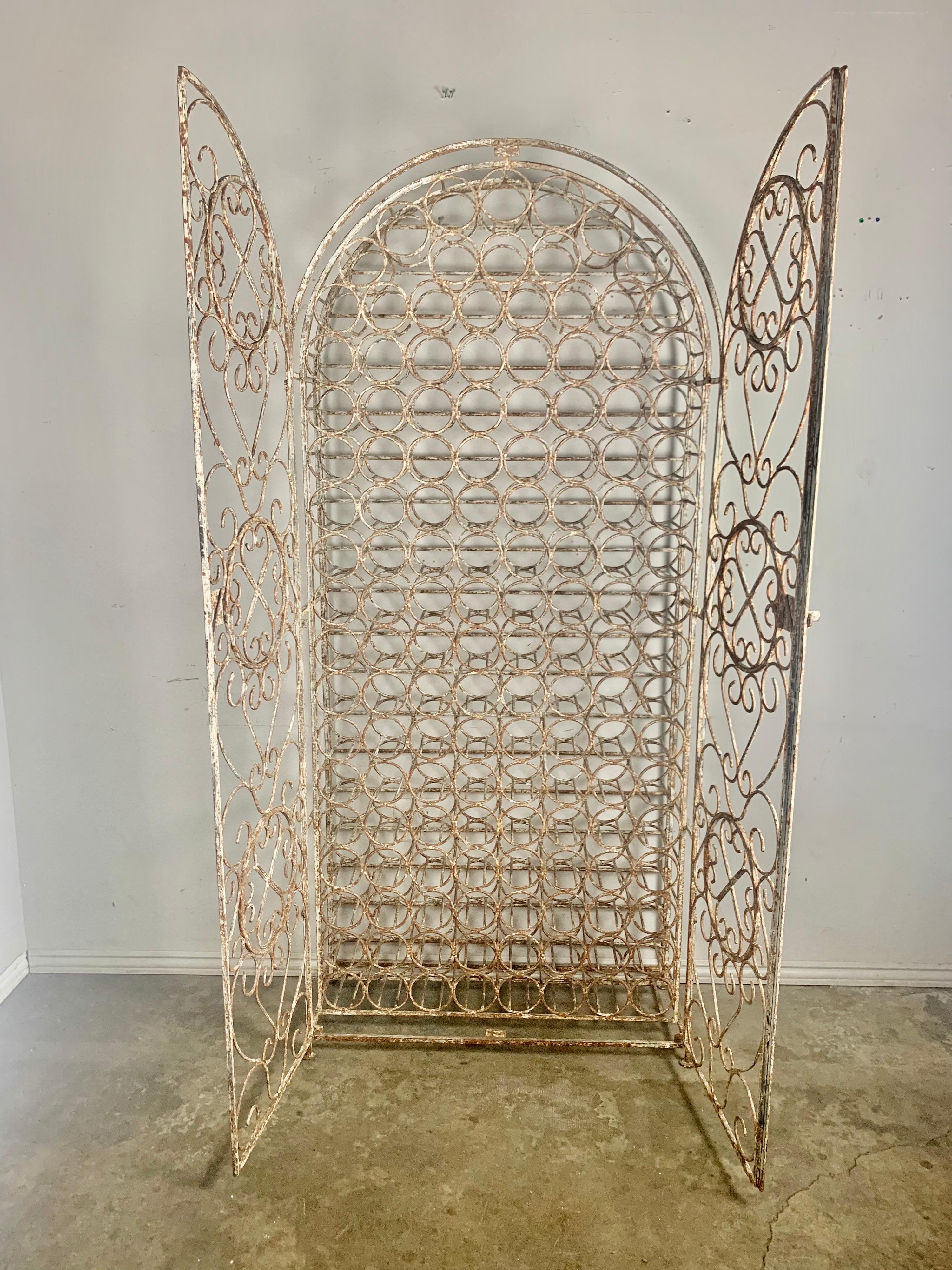 Wrought iron painted wine rack that holds 138 bottles of wine. This painted piece has developed a beautiful patina over the years. A pair of intricately hand forged doors open to reveal enough space to store your favorite wines. Great overall