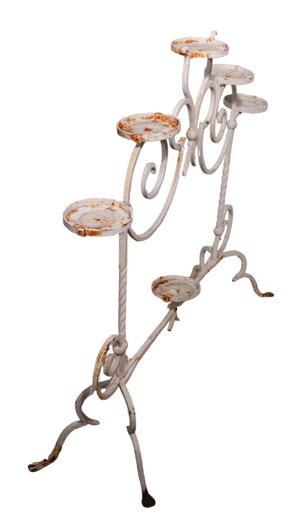 Charming Art Deco wrought iron plant stand having six disk form pot holder surfaces ( 5 in. diameter. ) with a decorative frame structure. The stand is in very good condition, free of breaks, damage or repairs. Currently in later, but not new, white