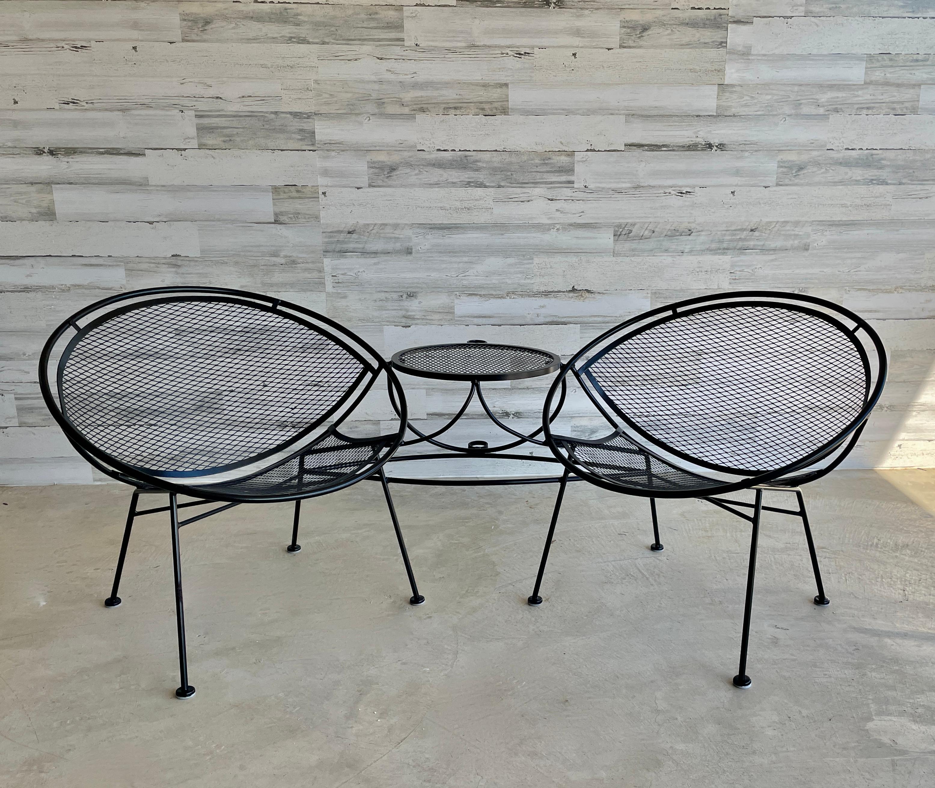 Vintage 1950s wrought iron 'tête-à-tête'. Designed by Maurizio Tempestini for Salterini. The two lounge chairs are connected by a table between, which also incorporates an umbrella holder.