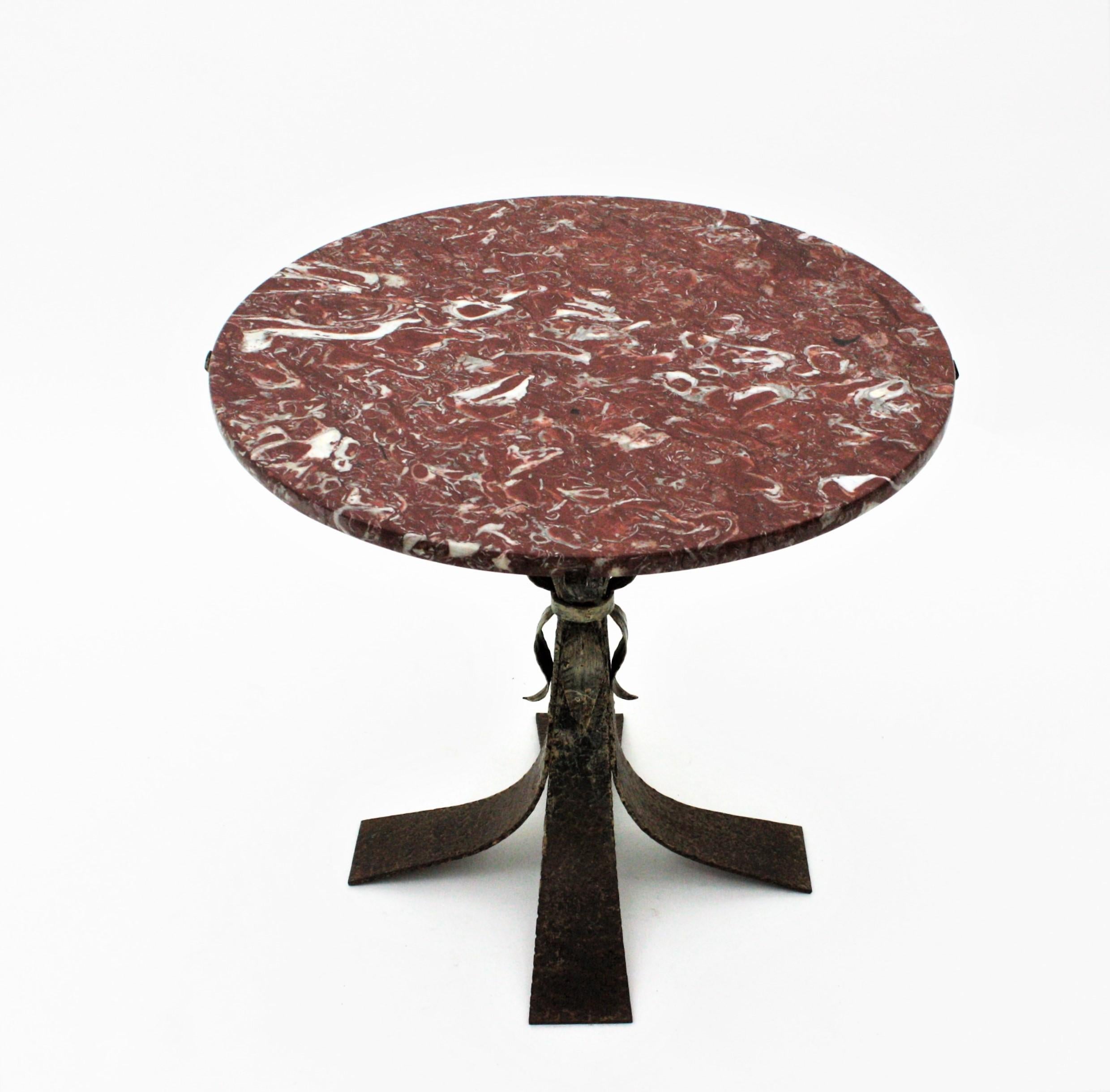 Eye-catching Mid-Century Modern wrought iron low table with garnet and white marble top. Spain, 1950s.
This side table has a beautiful spotted marble top standing up on a wrought iron four feet base with leaf details. It retains rests of its