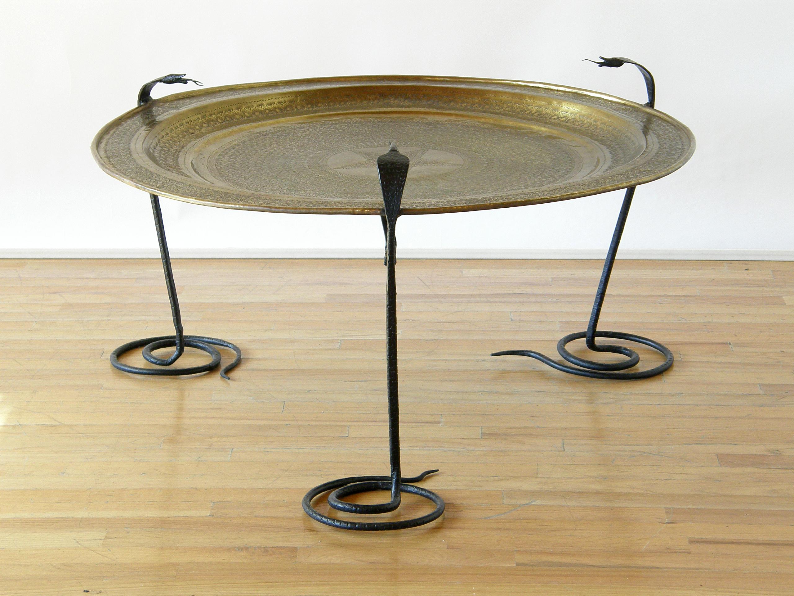 This unique table has handwrought iron serpents for legs. Their coiled tails form their bases, then their heads rise up above the surface of the table. Their necks flare like Egyptian cobras, and their forked tongues flicker from their open mouths.
