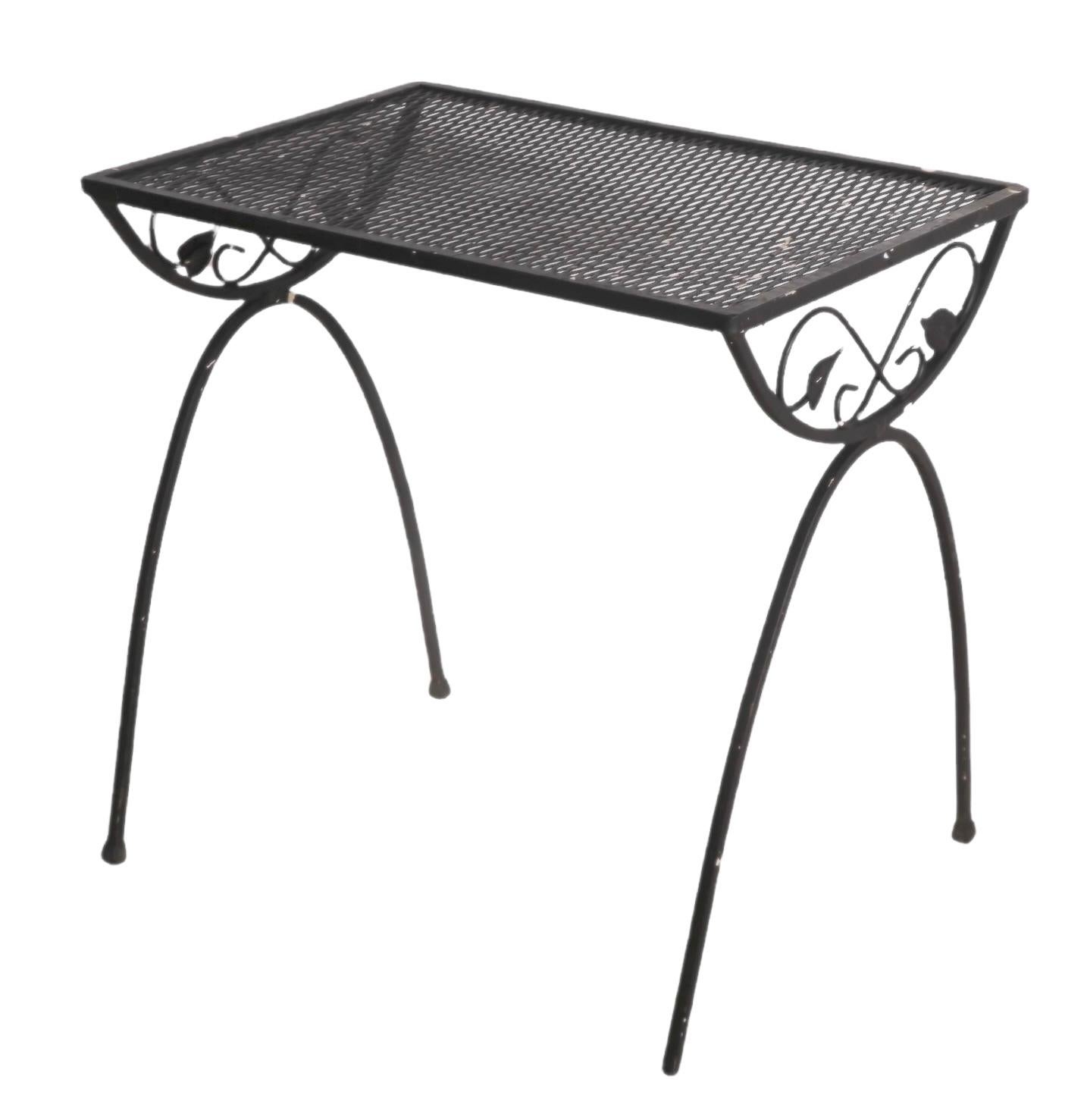 Garden, patio, poolside or sunroom side table having arched legs and top support, and a metal mesh top. Probably by Woodard, unsigned. The table is structurally sound and sturdy, the black paint finish shows wear, and some plastic feet are missing.