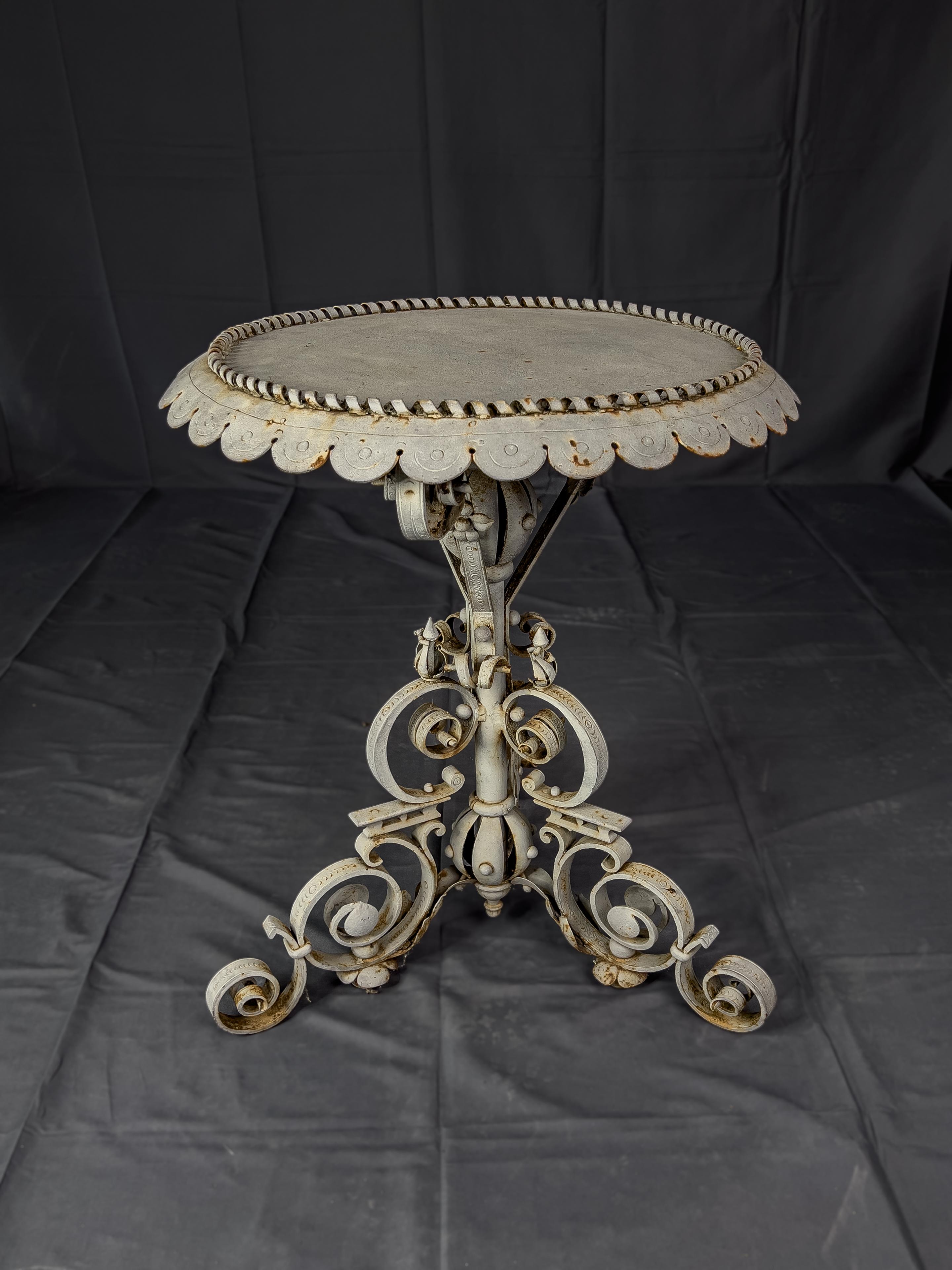 Baroque style painted wrought iron side table with a tripod pedestal base that has elaborate turned and stamped decoration. The side table has a scalloped edge top and a twisted metal gallery rail.  This is a unique table which makes a great 