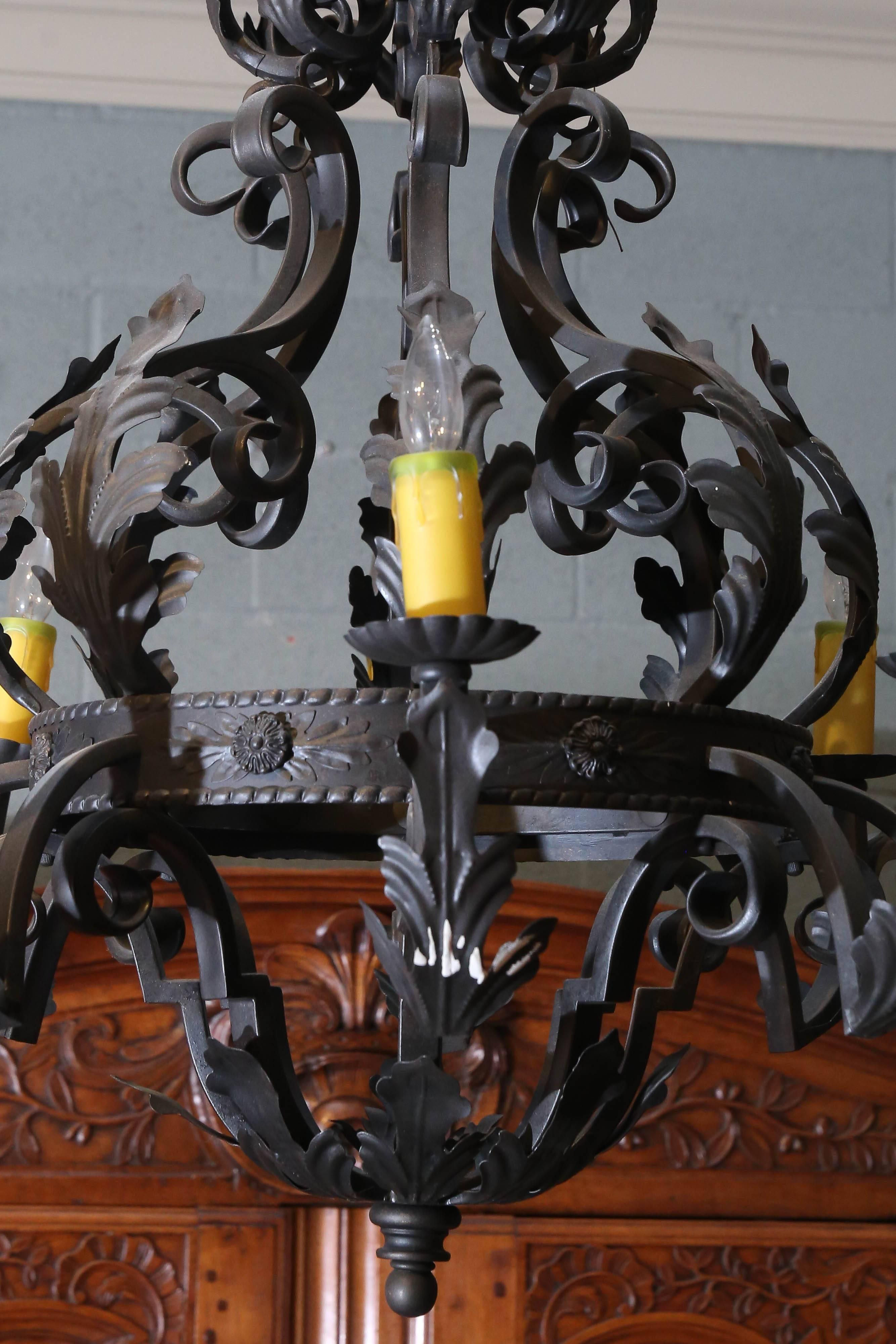Spanish-style wrought iron has eight arms with melon-shaped bobeche and acanthus leaves attached to a centre band that is embossed and features casts rosettes.

From top of band are more acanthus leaves with more at top and bottom of
