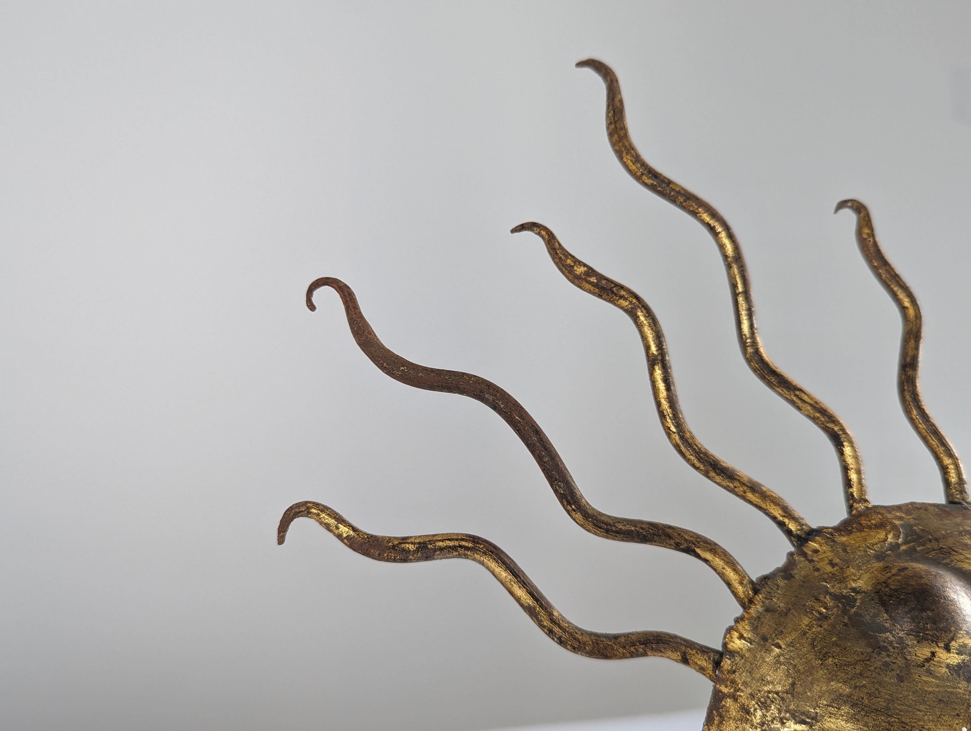 This exquisite gold gilt iron lamp, featuring a hand-hammered Sunburst design, comes in a rare and compact size. Inspired by the style of Gilbert Poillerat, this piece is richly decorated in the central part with distinctive hammer marks, enhancing