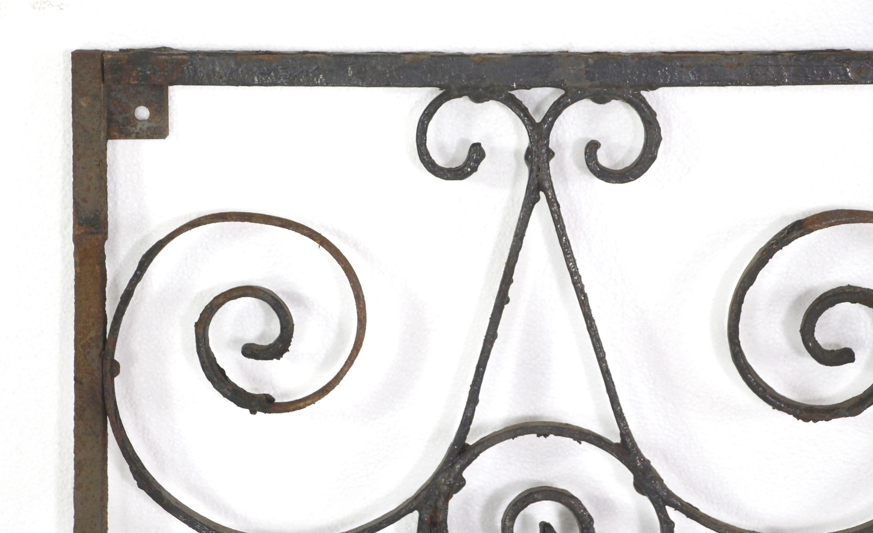 This antique wrought iron gate is hand forged with ornate swirled details and curls. It has a solid frame and is suitable for a gate or a variety of purposes such as a wall ornament or incorporated into a table with a glass top. There is rust from