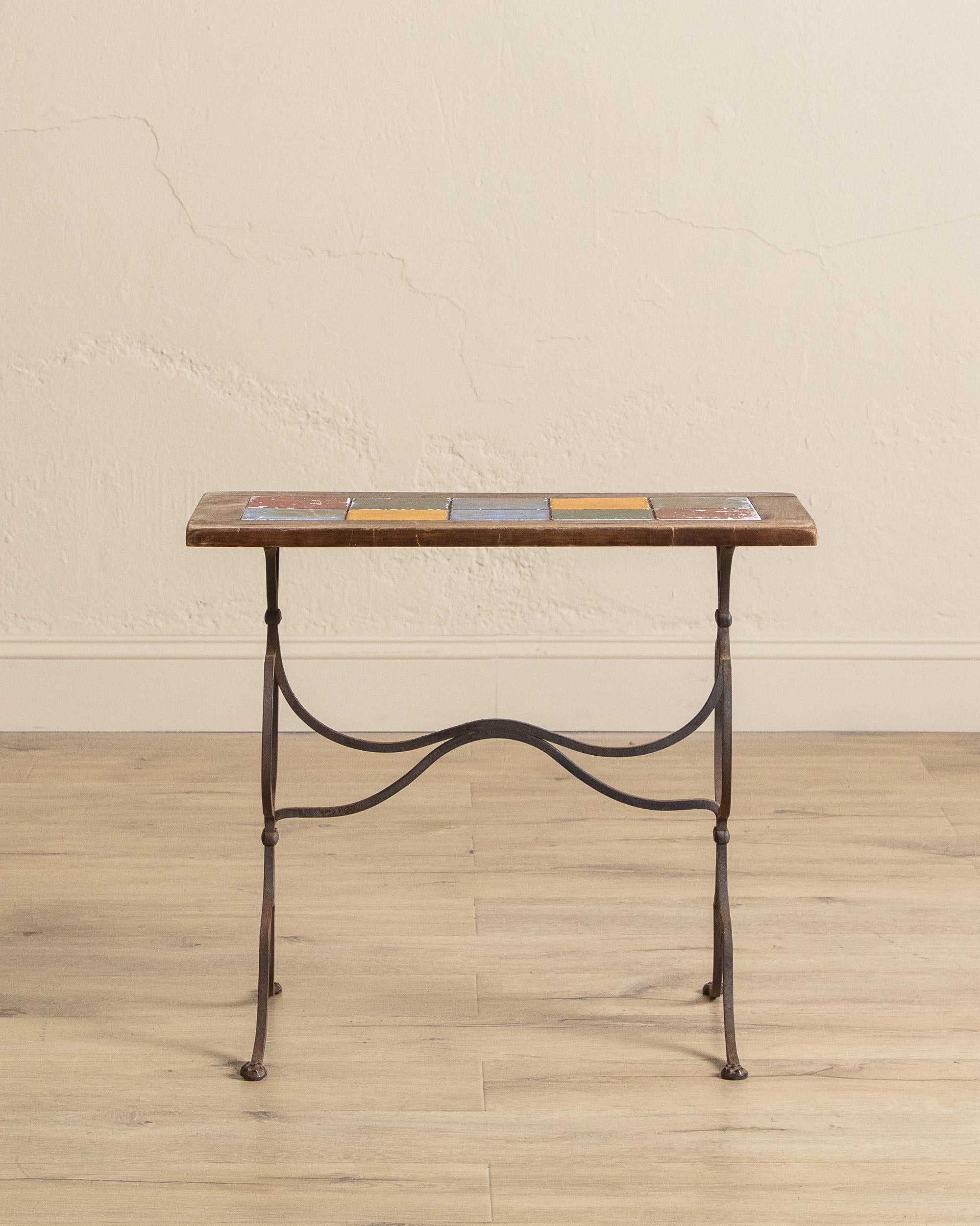 Cette table d'appoint en fer forgé, datant probablement du milieu du XXe siècle, présente un plateau en carreaux de faïence vibrant associé à une patine magnifiquement vieillie, offrant un jeu saisissant de couleurs et de textures. Les carreaux de