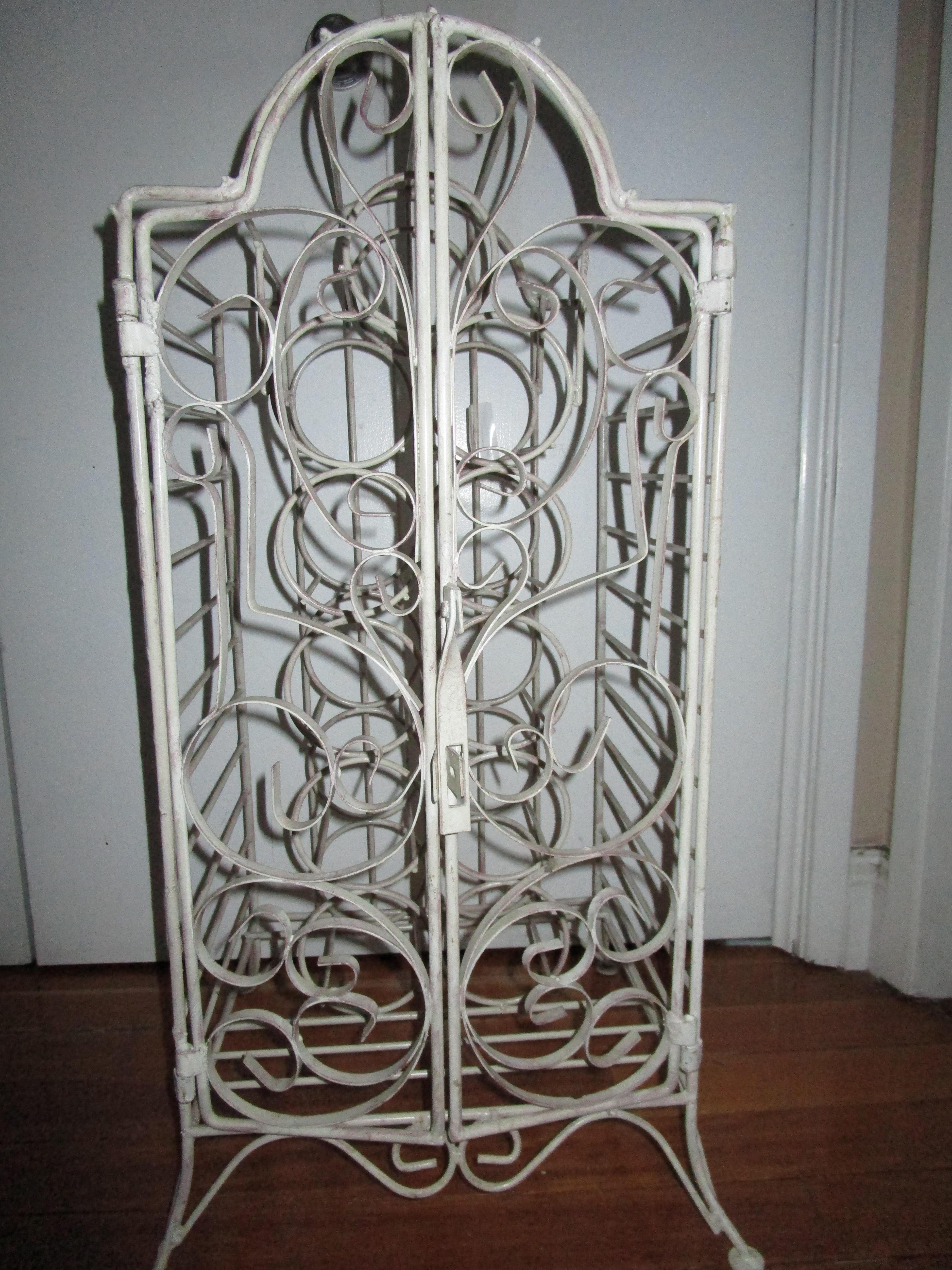 The intricate wrought iron pattern, the latch for private reserve and the French feel make this wine cabinet a standout. A vintage French style white-painted wrought iron wine cabinet from the mid 20th Century stands ready to accept your private cru
