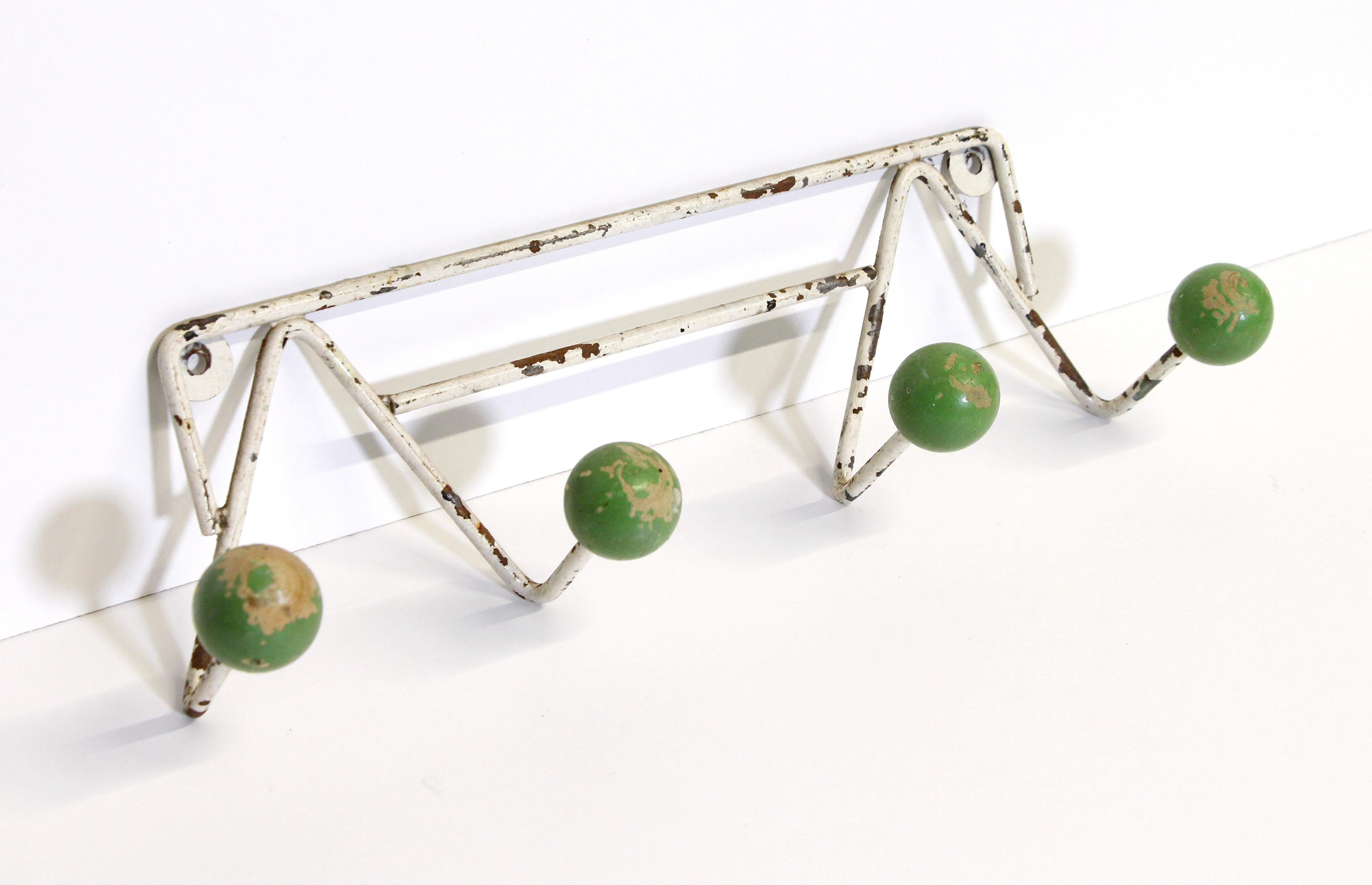 European Mid-Century Modern white wrought iron wall rack.  It features two double arms each holding a green wooden ball hook.  There is distressing in the paint from age giving it a shabby chic look.  This rack is imported from Belgium. This can be