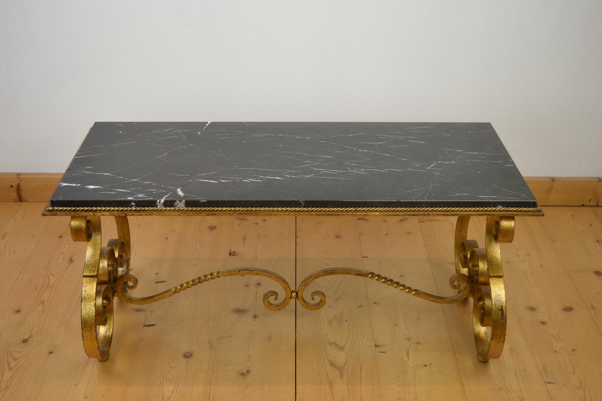 French coffee table of wrought iron with a marble top from the 1950s.
This great coffee table has a curled gilded wrought iron base with a polished black vained marble top or tray. Around the marble top you have a metal twisted cord.
A French coffee