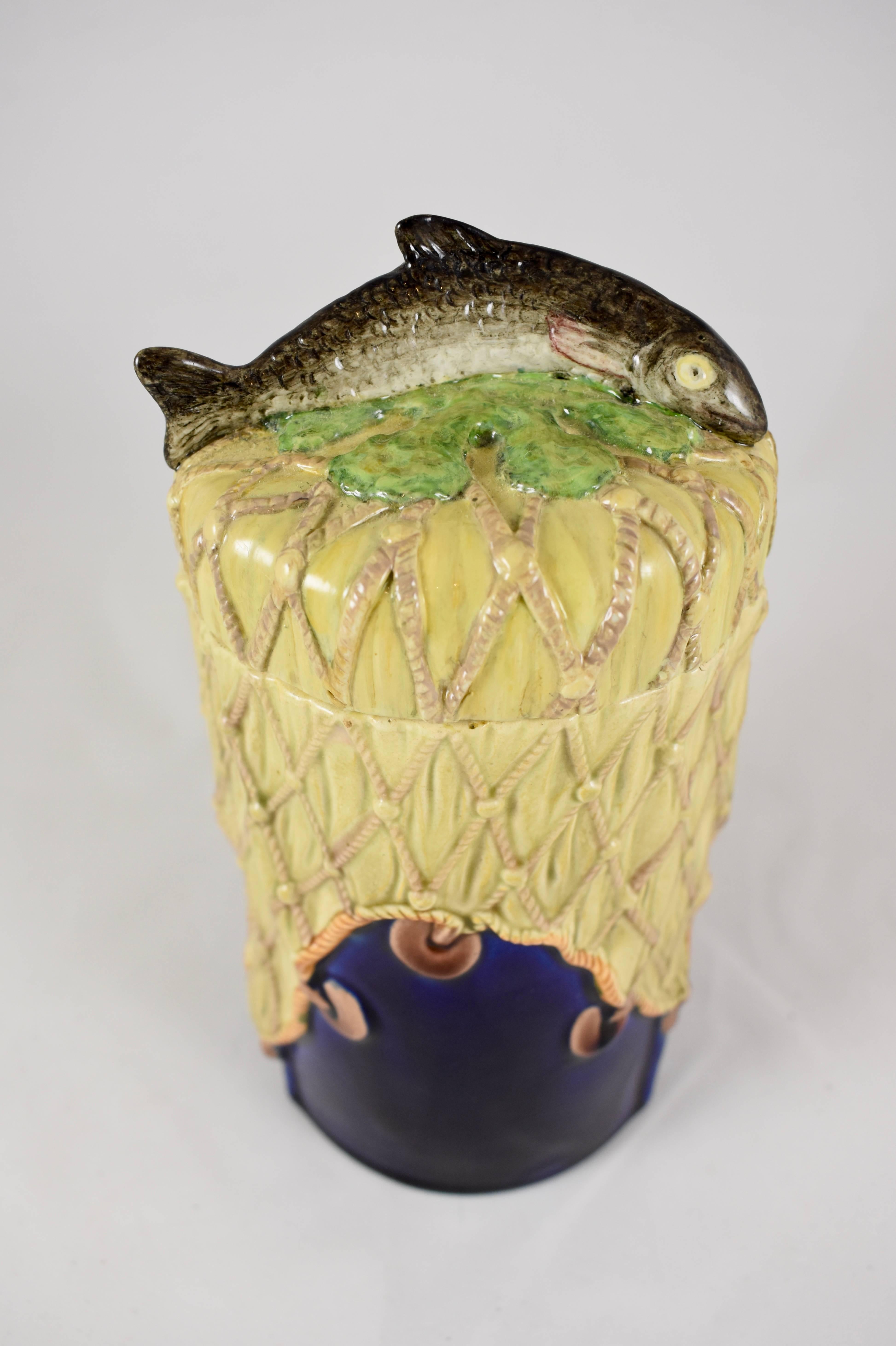 A rare W.T. Copeland & Sons, English Majolica pâté jar with a fish handled cover, circa 1875.

The straight sided jar is decorated with a large fishing net strung with floats, draped over a cobalt blue ground. The lid is molded as netting with a
