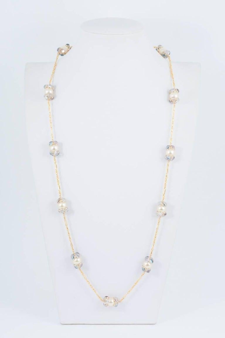 Un sautoir/ collier long délicat et ravissant,  avec des perles de lustre crème, chaque perle  coiffée de pétales en verre coulé lilas et aigue-marine, en haut et en bas, et d'une chaîne 