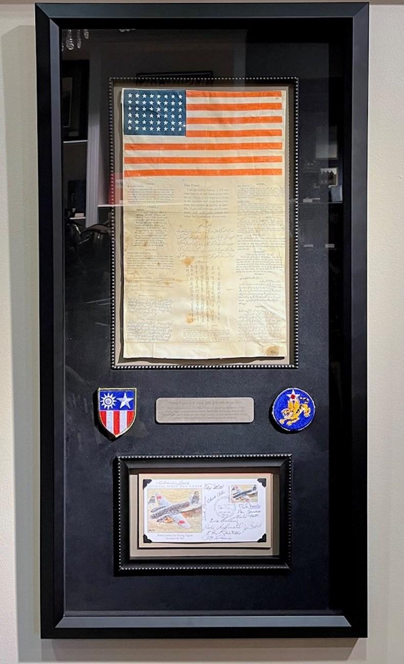 Presented is an original First Day Cover envelope signed by twelve members of the First American Volunteer Group, better known as the Flying Tigers. Accompanying the signed envelope are a silk 48-star WWII blood chit and embroidered Flying Tigers