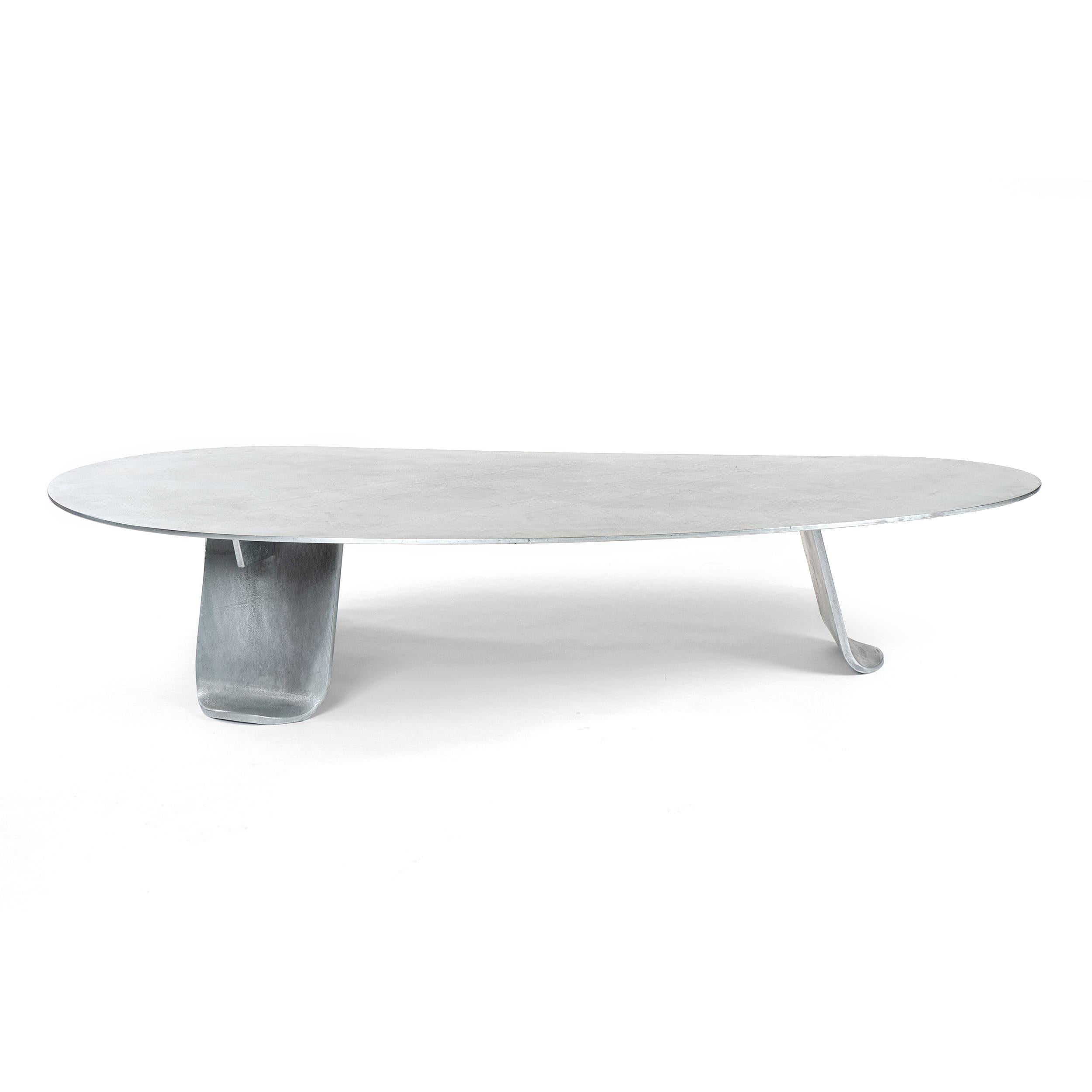 A low coffee / cocktail table of thick plate steel treated with a low sheen, hot zinc finish. The expansive, organically shaped top is set upon three wide, thick plate steel legs each having gradually tapering sides terminating in softened corners